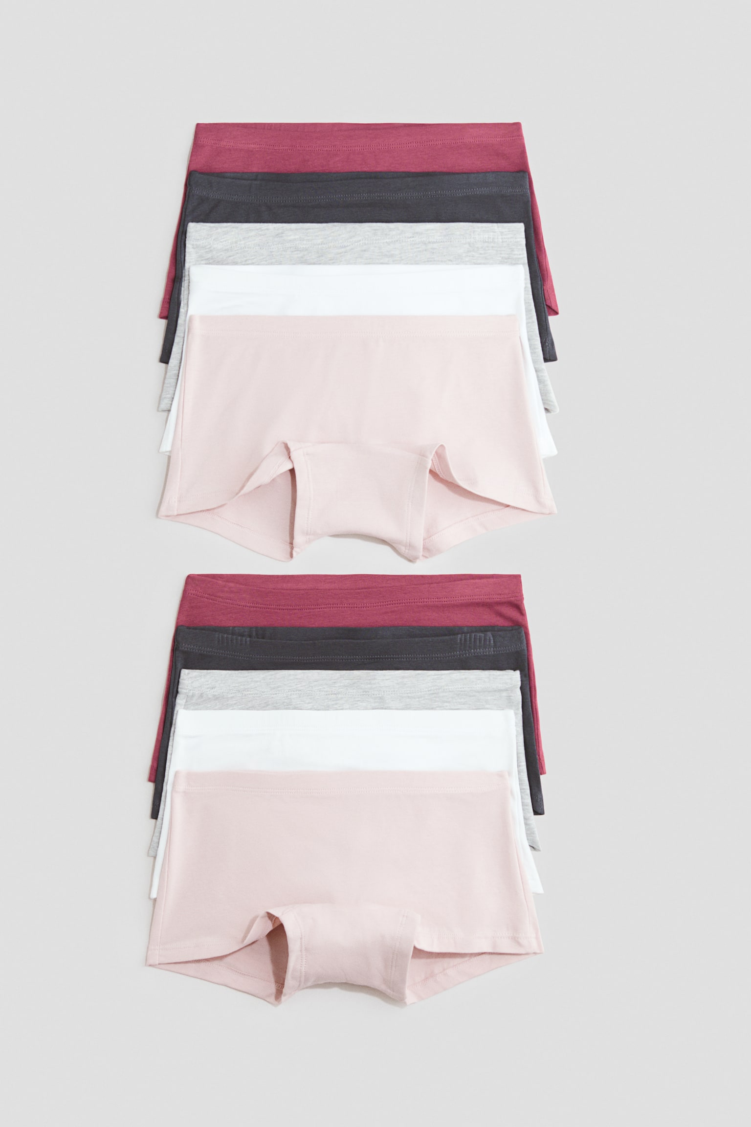 Two stacks of boyleg briefs in soft jersey are laid flat, each showing five pairs in dark red, dark grey, light grey, white, and light pink from the front. The design features an elasticated waistband and a lined gusset, visible on the top light pink pair.