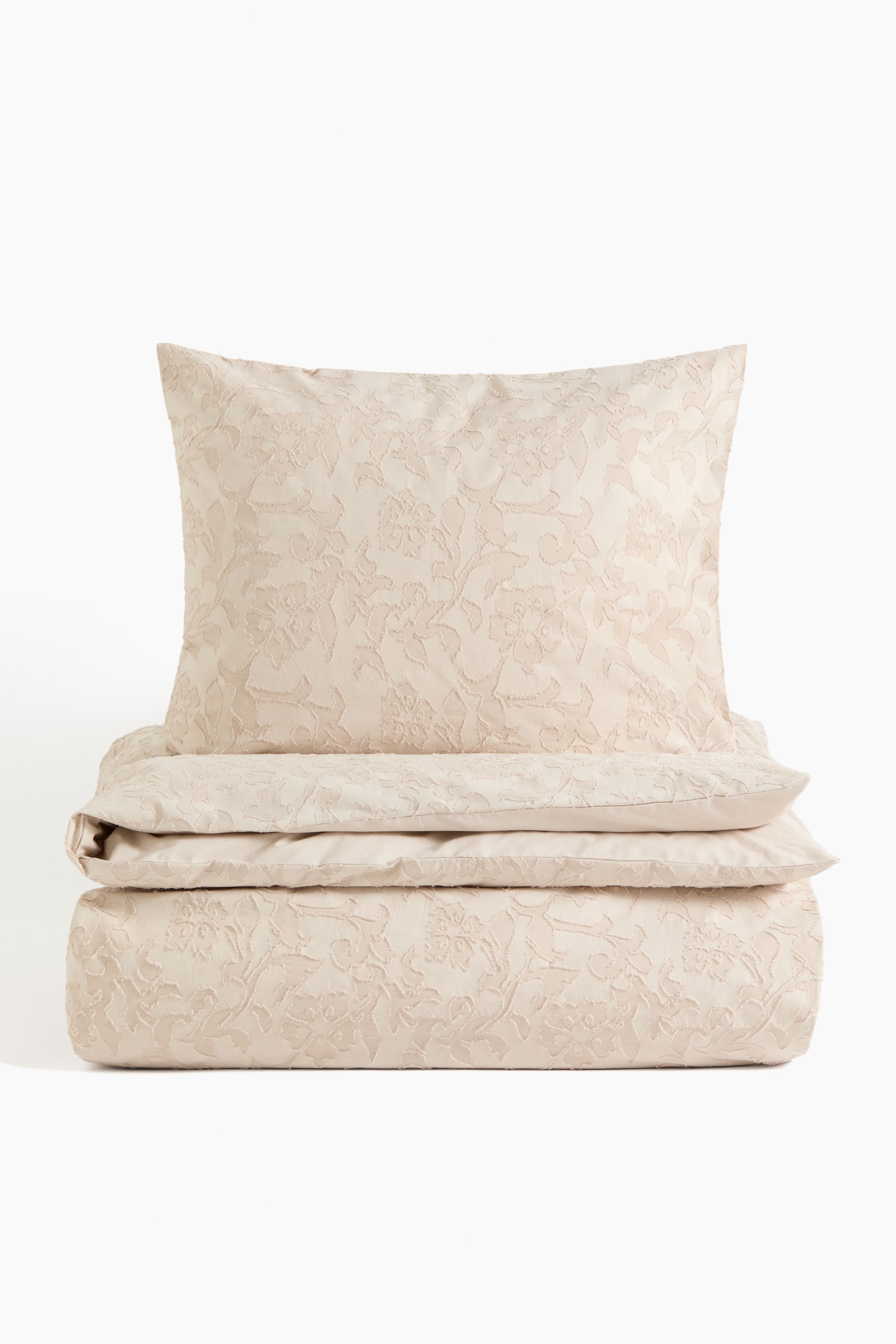 Voir une image plus grande: Un ensemble de housse de couette beige clair présente une taie d'oreiller en position verticale et une housse de couette pliée en dessous. Les deux pièces arborent un motif jacquard floral subtil et en relief sur toute leur surface.