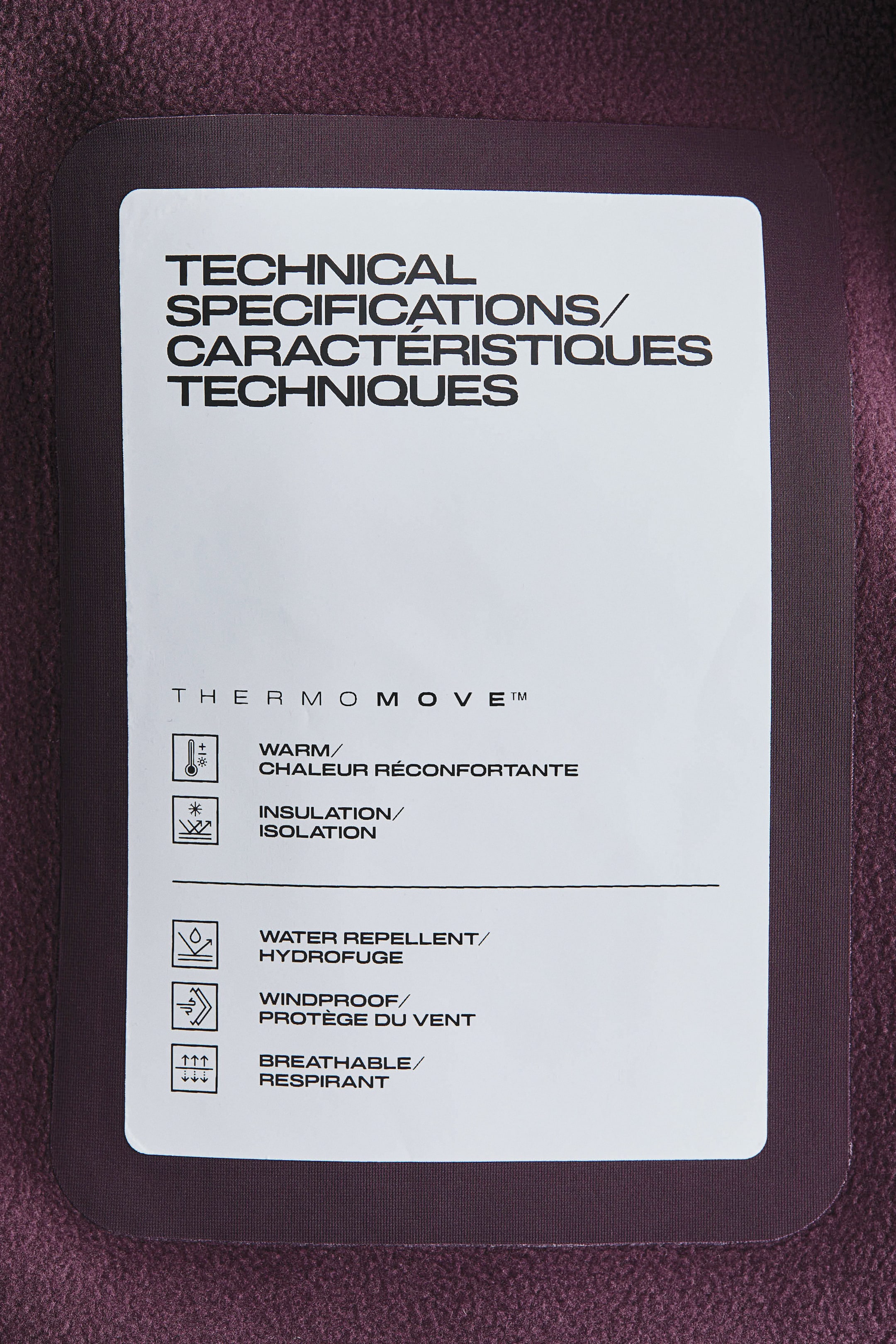 Agrandir l'image: Un pantalon de ski présente une étiquette de spécifications techniques blanche sur son tissu texturé violet foncé. L'étiquette met en avant des propriétés clés telles que la chaleur, l'isolation, la déperlance, la protection contre le vent et la respirabilité avec des icônes correspondantes, affirmant leur design fonctionnel.