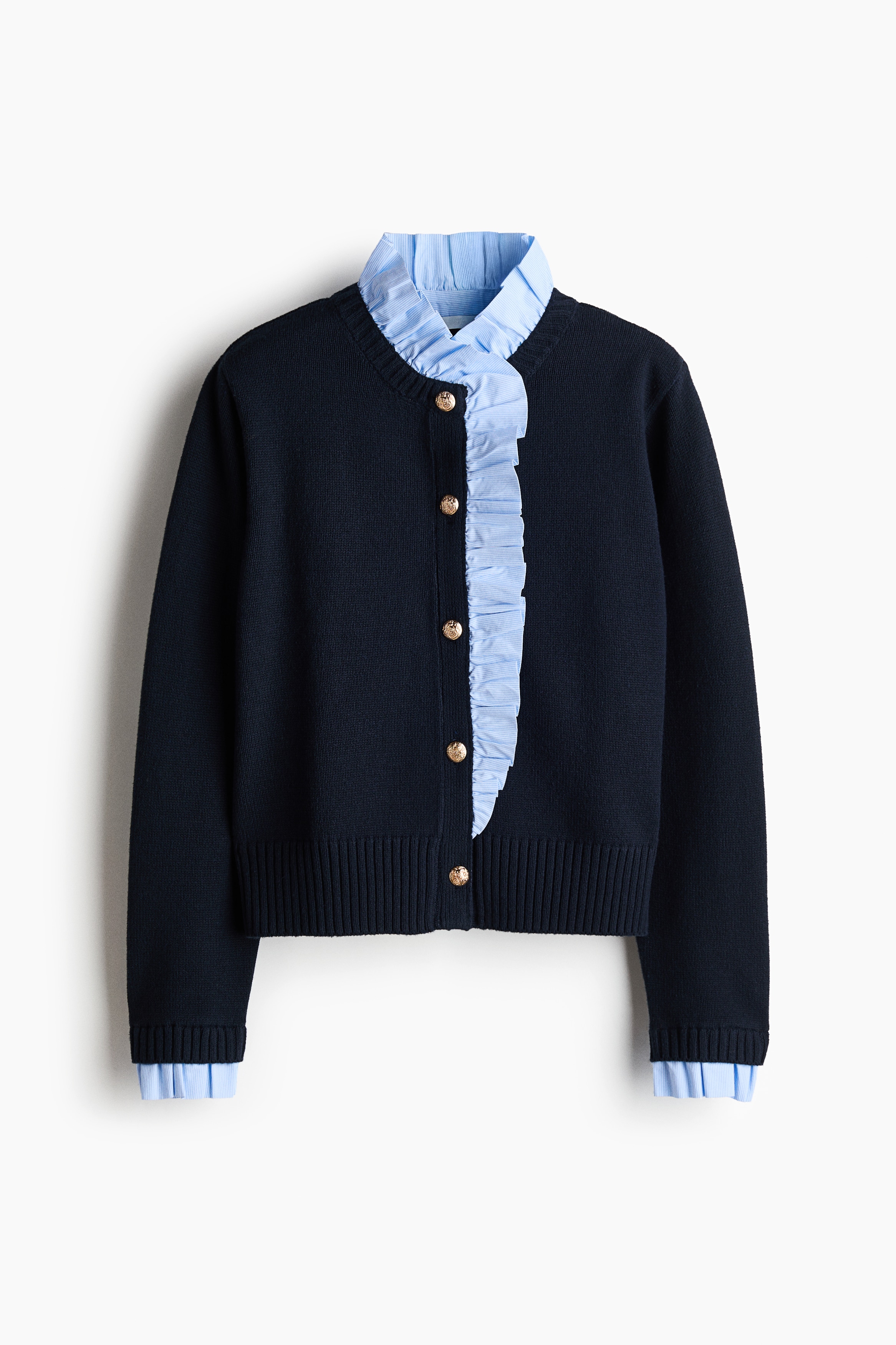 Vue rapprochÃ©e de face dâun cardigan en maille foncÃ©e, mettant en valeur une bordure Ã  volants en coton bleu clair et blanc rayÃ© le long de lâencolure cÃ´telÃ©e et de la patte de boutonnage. Le cardigan prÃ©sente des boutons ronds en mÃ©tal texturÃ© de ton dorÃ© et est superposÃ© Ã  un t-shirt blanc uni.
