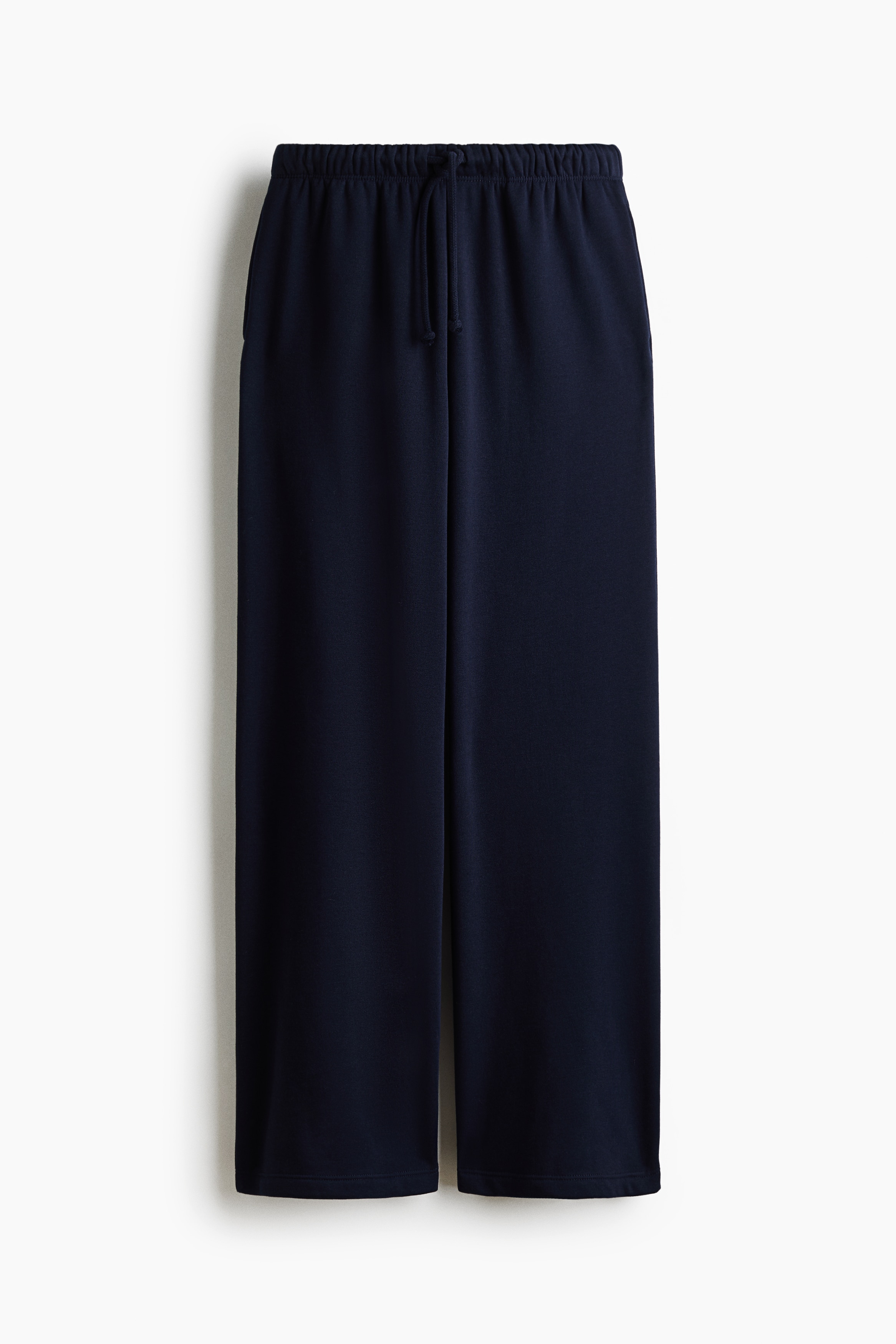 Weit geschnittene, locker sitzende Jogginghose in Dunkelmarine, getragen vom Model, mit sichtbarem elastischem Bund und Kordelzug. Die Hose ist mit einem weiÃen Cropped-Top und einem offen getragenen grauen Zip-Hoodie kombiniert.
