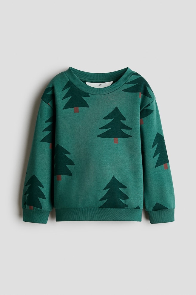 En grÃ¶n sweatshirt visas framifrÃ¥n och har ett tryckt motiv av mÃ¶rkgrÃ¶na tallar med bruna stammar. Sweatshirten har en rund ribbad halsringning, sÃ¤nkta axlar, lÃ¥nga Ã¤rmar med ribbade muddar och en ribbad nederkant. - 1