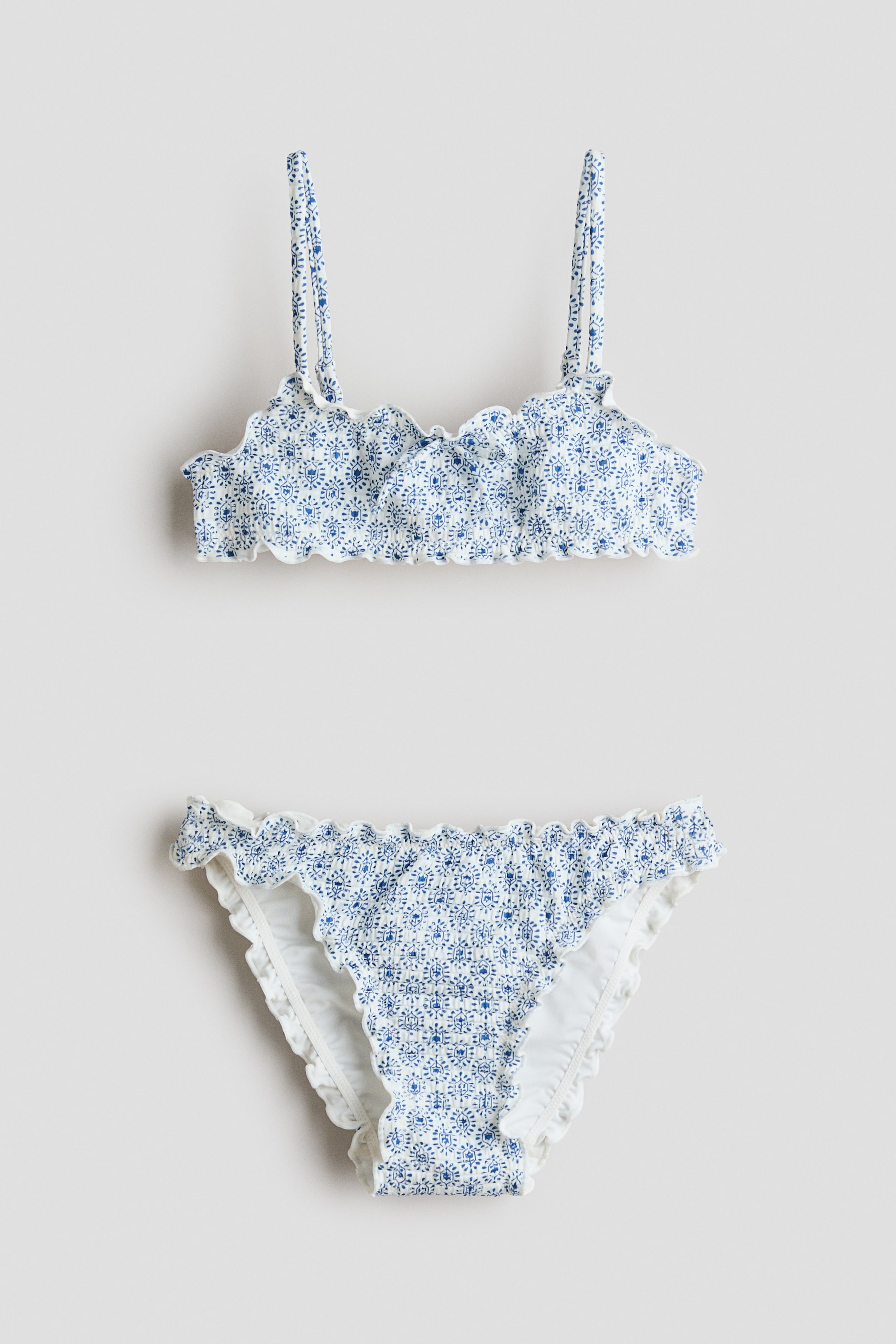 Agrandir l'image: Un ensemble bikini face avant présente un haut à motifs bleus et blancs avec un tissu froncé, des bretelles étroites et réglables, et un nœud cousu à l'avant central, assorti à un bas froncé ; les deux pièces sont dotées de bords festonnés surjetés.