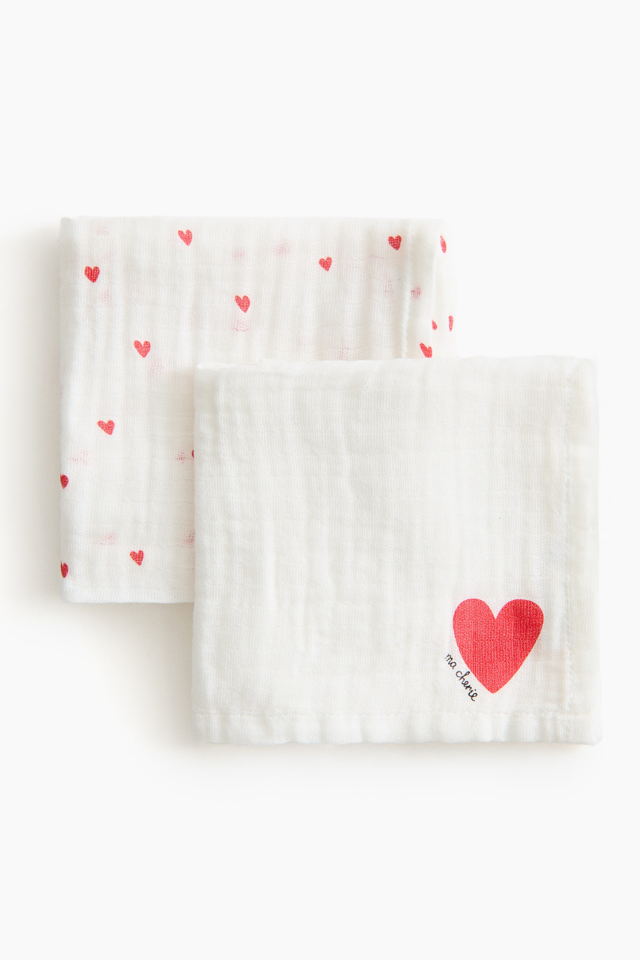 Ver imagen más grande: Se presentan dos muselinas de algodón, dobladas y superpuestas. La muselina en primer plano presenta un gran diseño de corazón rojo con el texto 'ma cherie', mientras que la muselina parcialmente visible detrás muestra un patrón de corazones rojos más pequeños y dispersos.