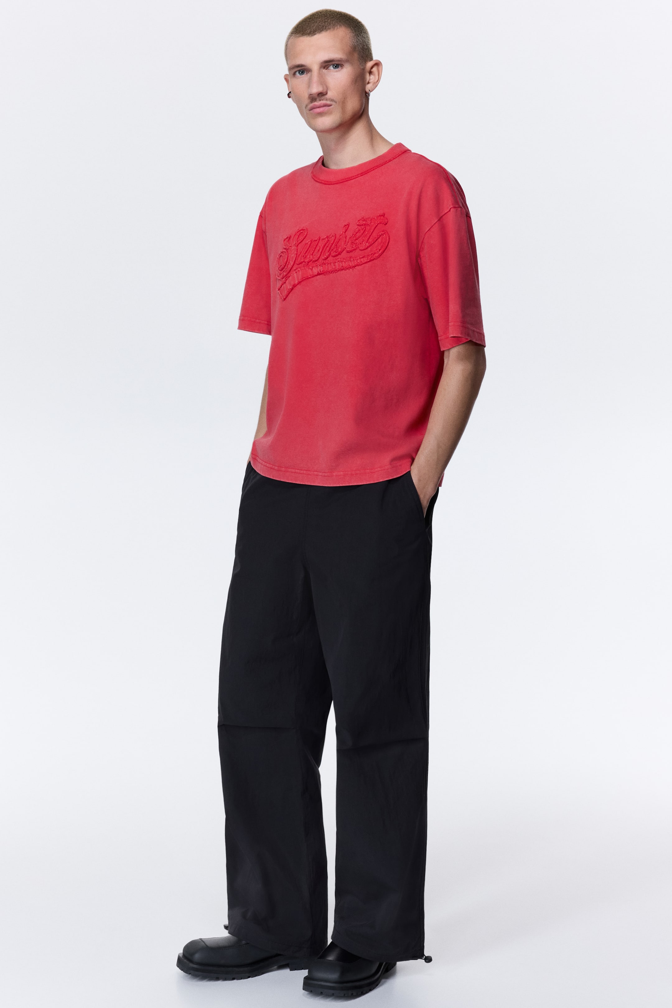 Xem ảnh lớn hơn: Áo thun dáng rộng với tông đỏ washed, tay ngắn. Thiết kế cổ tròn, điểm nhấn là họa tiết chữ nổi, bề mặt có texture “Sunset” ở phía trước ngực.