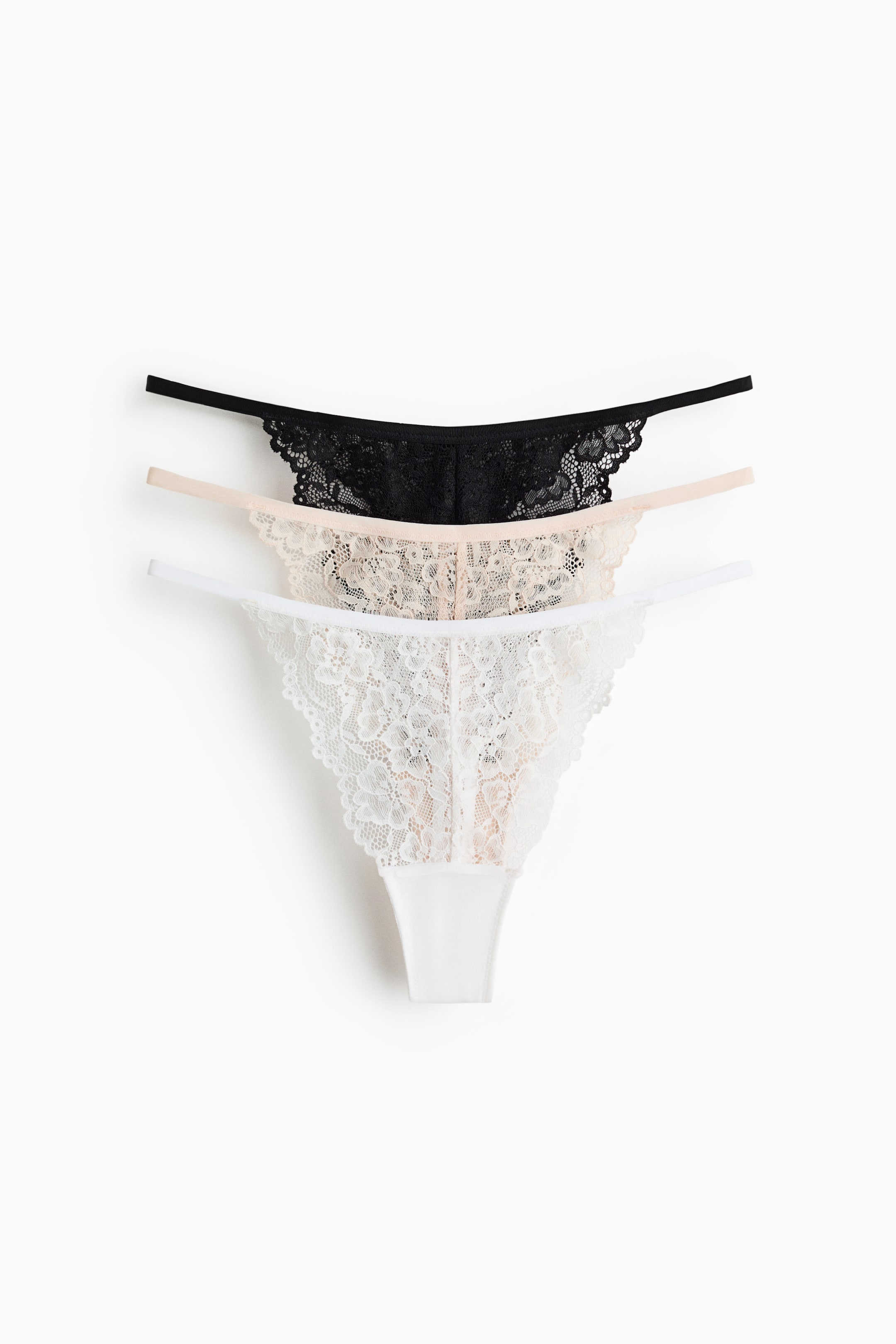 Grotere afbeelding bekijken: Drie string slips worden weergegeven, elk gemaakt van kant met een lage taille, smalle zijkanten en een gevoerd kruisje. Ze verschijnen in zwart, licht perzik en wit, gestapeld met hun voorkanten zichtbaar.