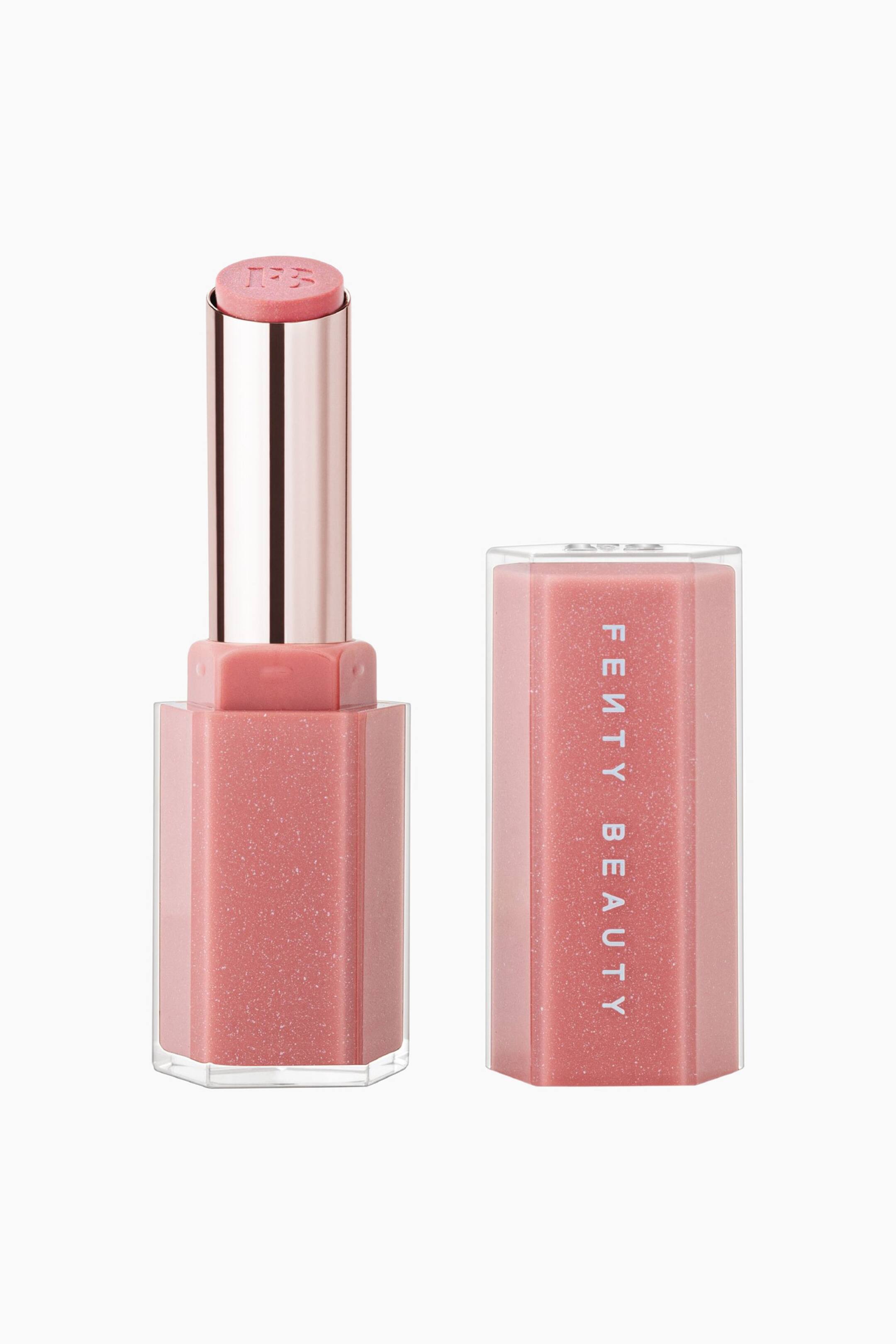 Näytä suurempi kuva: Gloss Bomb Stix High-shine Shimmer Gloss Stick seisoo pystyasennossa sen yhteensopivan korkin vieressä, tuoden esiin sen etupuolelle suunnatun muotoilun. Avattu hylsy paljastaa kiinteän, kimaltelevan vaaleanpunaisen glossin, johon on kohokuvioitu ”FB”-logo, kun taas viereinen kuusikulmainen korkki näyttää ”FENTY BEAUTY” -logon pystysuunnassa valkoisella painettuna.