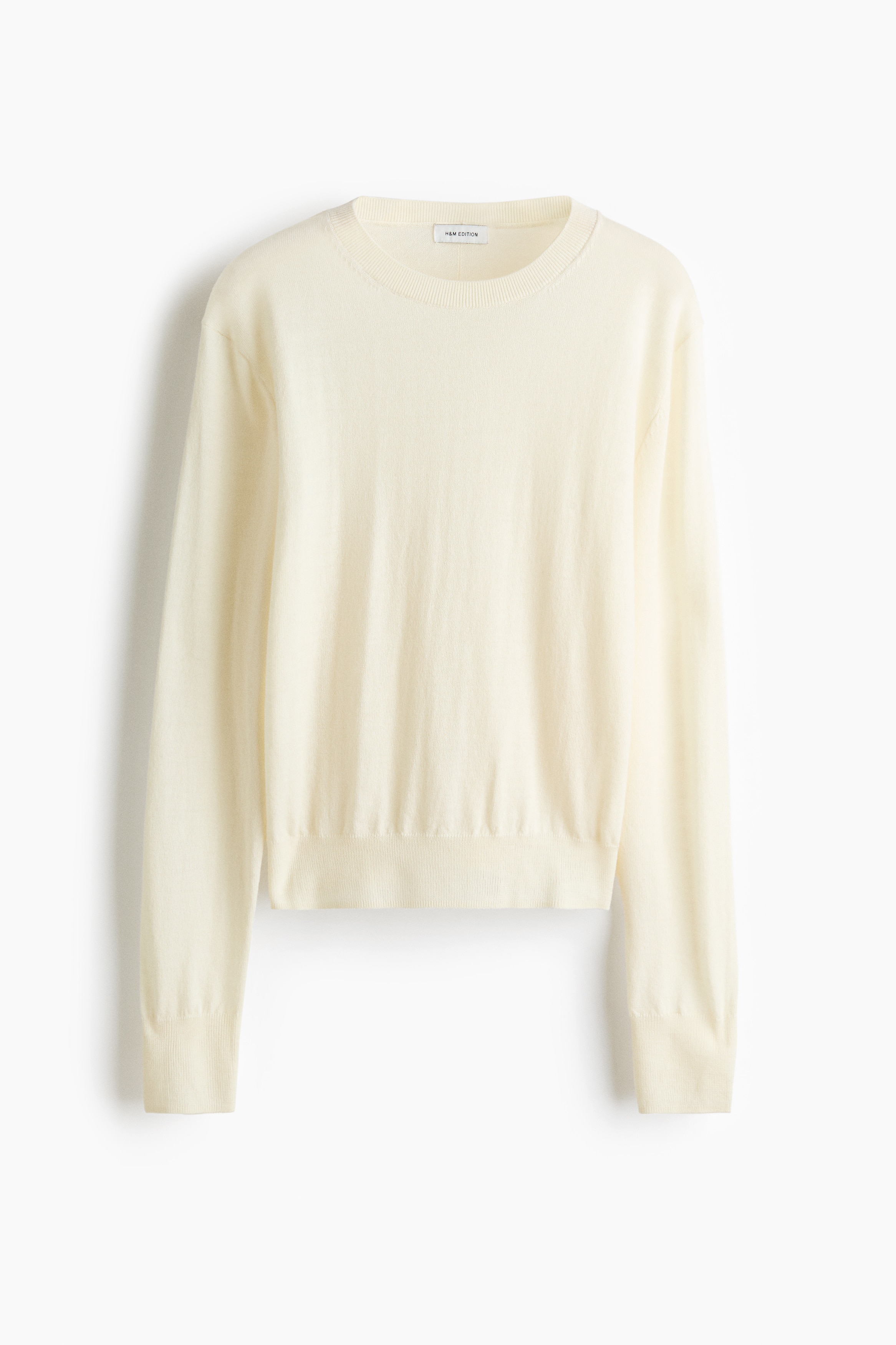 A cream-coloured knitted wool jumper featuring dropped shoulders and long sleeves with ribbed cuffs is being worn by the model. The jumper is tucked into a structured, high-waisted black leather skirt.