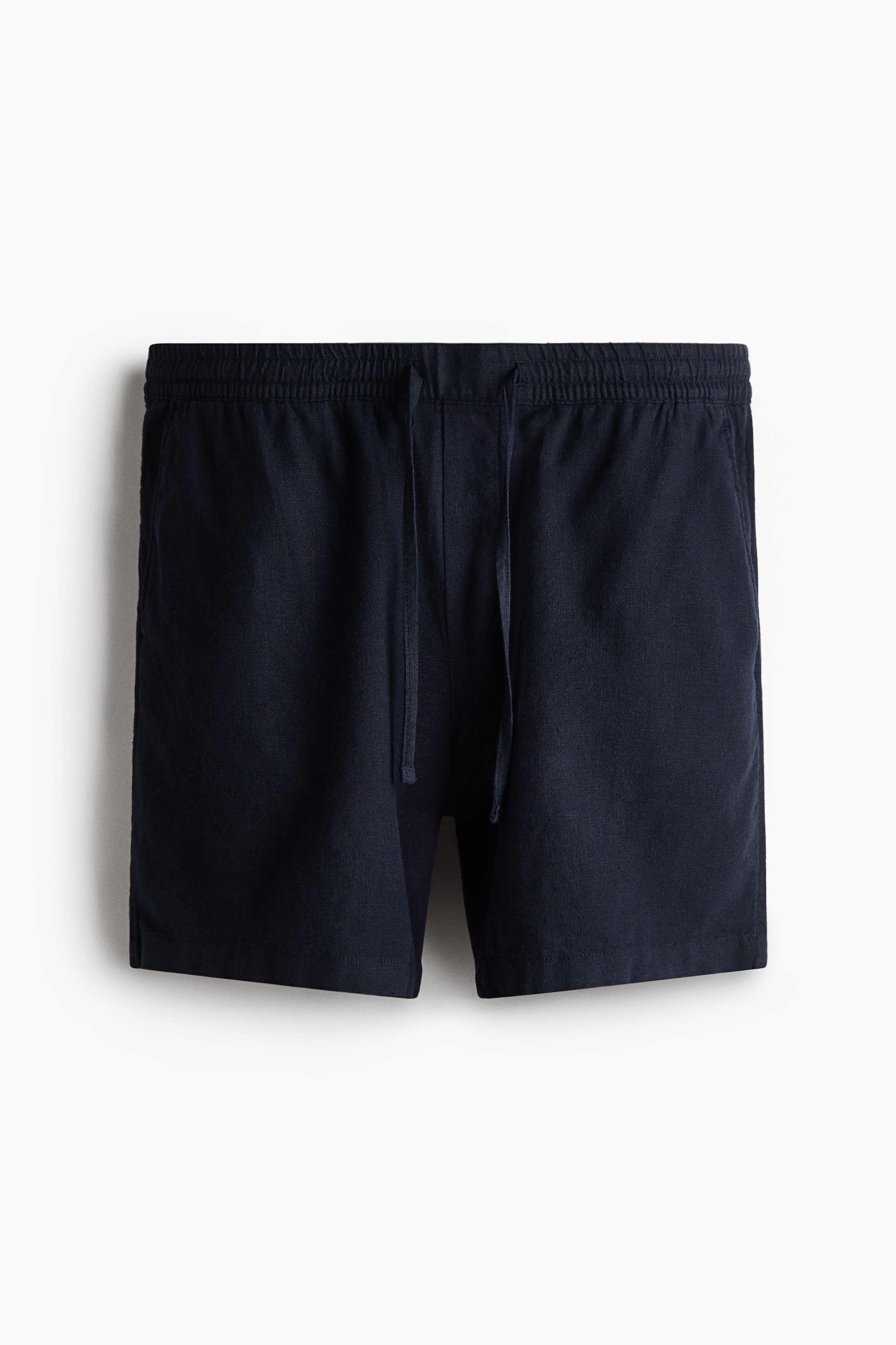 View larger image: A pair of dark blue shorts is showcasing a front view, crafted from a breezy linen and viscose blend. They feature a covered elasticated waist with a drawstring, a faux fly detail, and diagonal side pockets, offering a relaxed fit.
