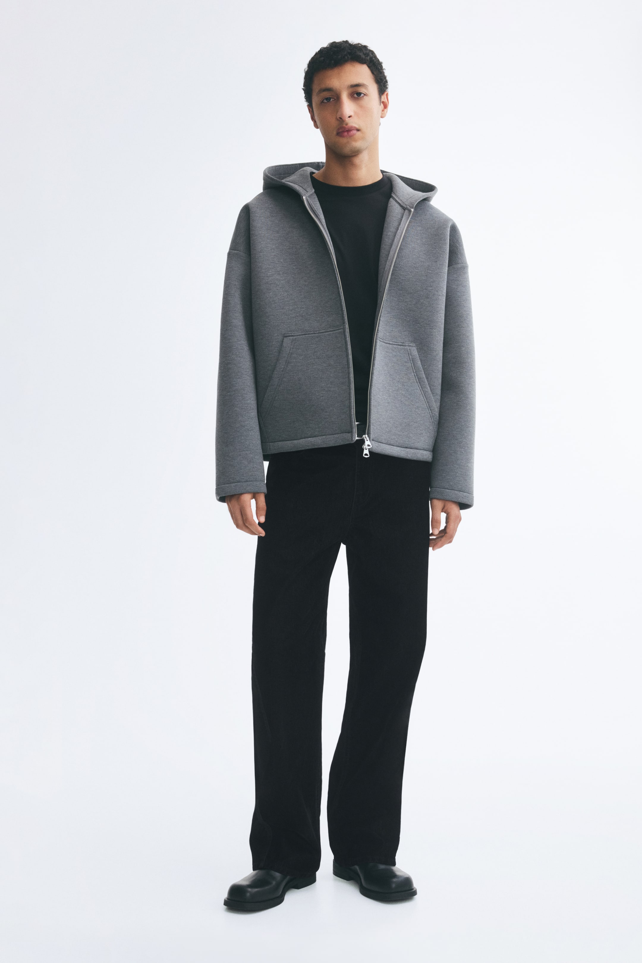 View larger image: Black 5-pocket trousers in a flocked cotton twill are being worn by the model, showcasing a relaxed fit and straight legs. The trousers are being paired with a grey zip-up hoodie, a black T-shirt, and black leather boots.