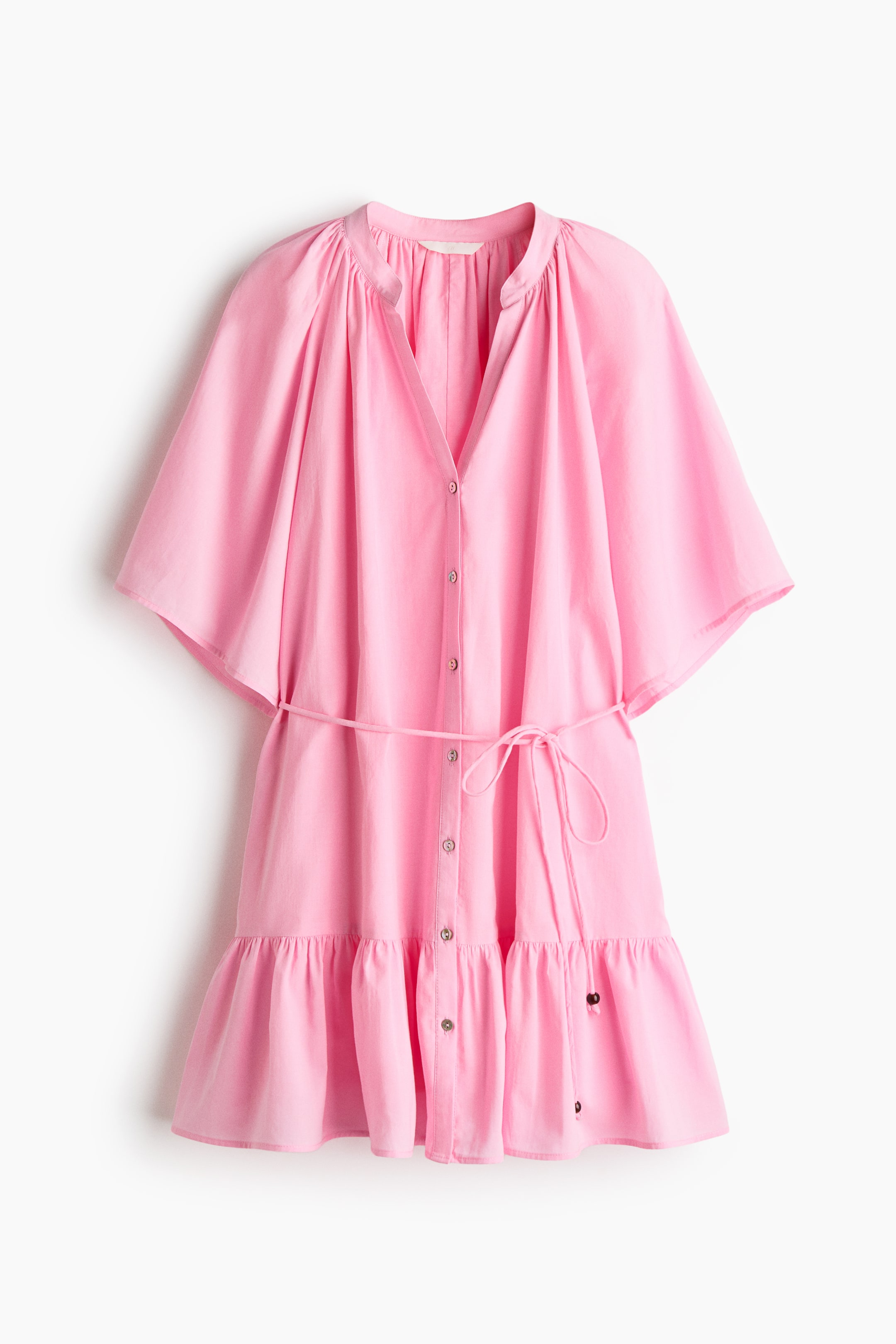 View larger image: A pink short dress is shown from the front, featuring a gathered band collar and a V-shaped opening. Buttons run down the front, and it is styled with short raglan sleeves, a spaghetti tie belt at the waist, and a flared skirt with a gathered tier.