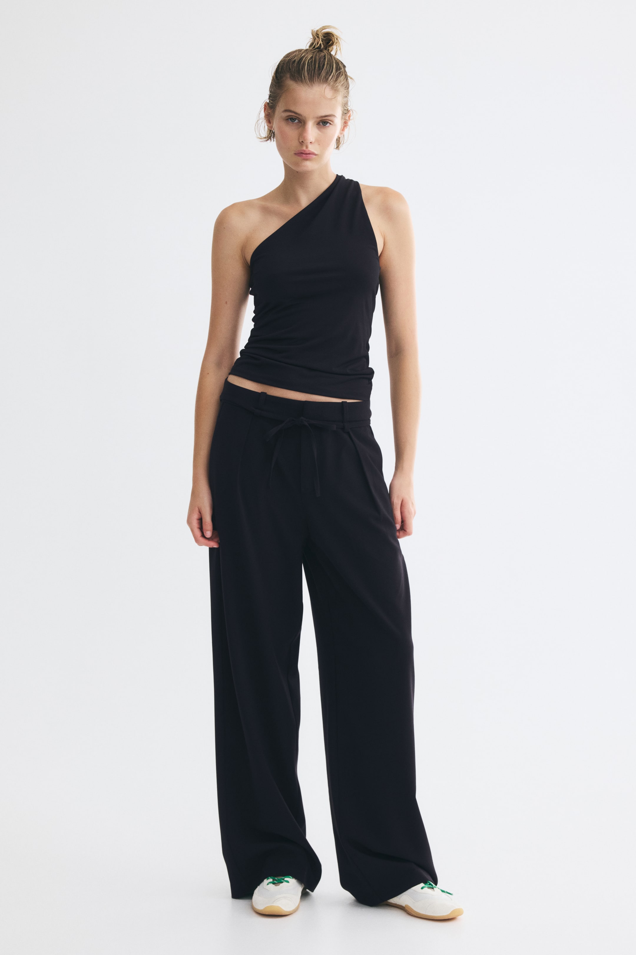 Größeres Bild anzeigen: Die schwarze Hose mit hoher Taille wird vom Model getragen und verfügt über einen gebundenen Bindegürtel in der Taille, dezente Seitentaschen sowie vorne sichtbare Bügelfalten an den geraden Beinen.
