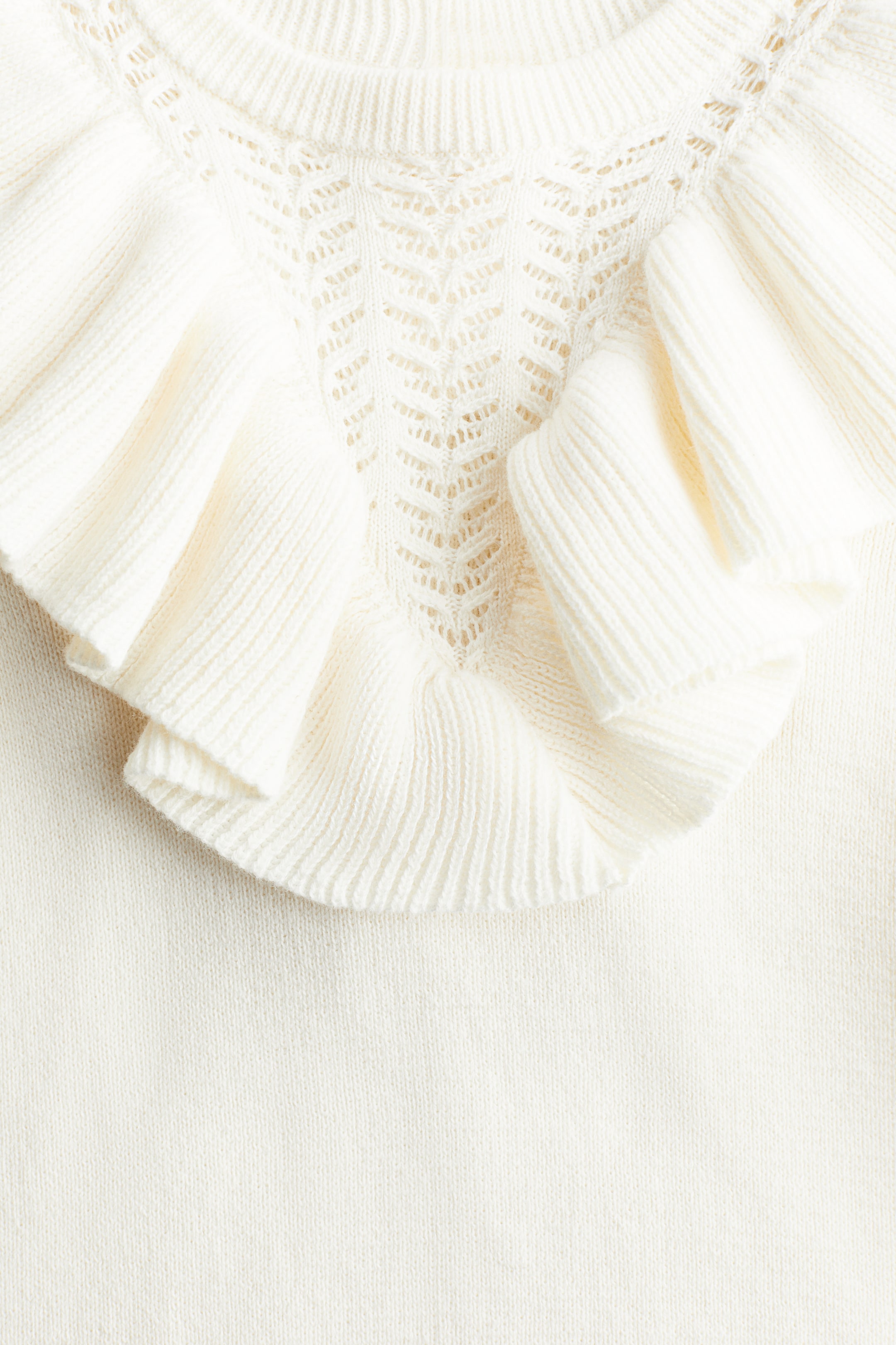 拡大画像を表示: H&Mアドーラブルズドレスは、丸いリブトリムのネックラインを特徴とする上部のフロントを展示しています。V字型のヨークにはオープンワークのニットパターンが見られ、肩にかけてボリュームのあるフラウンスが広がっており、すべてが柔らかく細かいニットで作られています。
