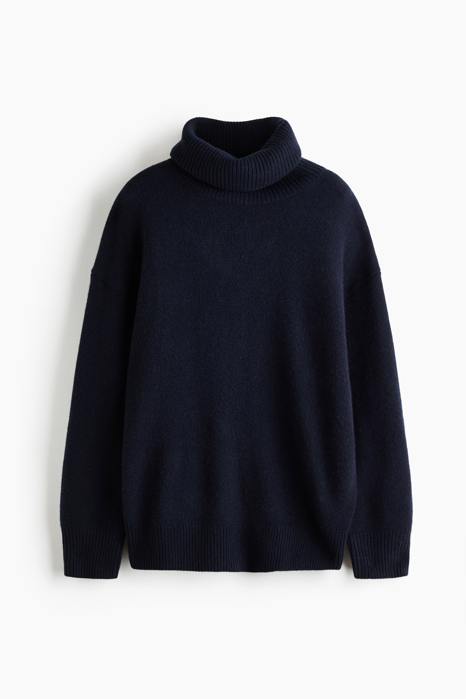 PÅednÃ­ pohled na oversized pletenÃ½ svetr v tmavÄ nÃ¡moÅnickÃ© modrÃ© barvÄ, s vÃ½raznÃ½m Å¾ebrovanÃ½m rolÃ¡kem a spadlÃ½mi rameny. Design zahrnuje dlouhÃ© rukÃ¡vy se Å¡irokÃ½mi Å¾ebrovanÃ½mi manÅ¾etami a sladÄnÃ½m Å¡irokÃ½m Å¾ebrovanÃ½m spodnÃ­m lemem.