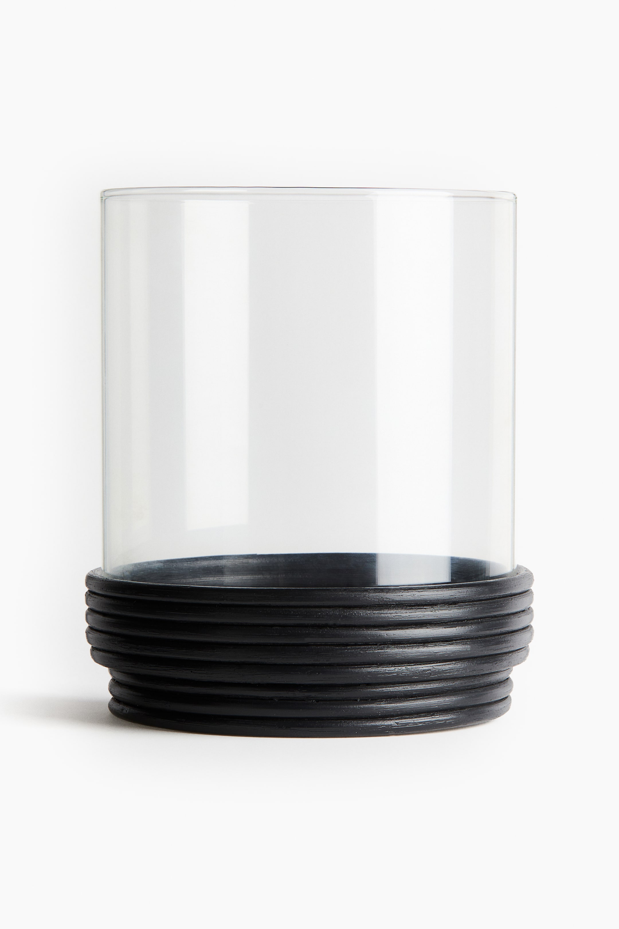 Voir une image plus grande: Un porte-verre cylindrique est positionné face à l'avant, avec une section supérieure en verre transparent et une base noire ornée de nervures concentriques horizontales.