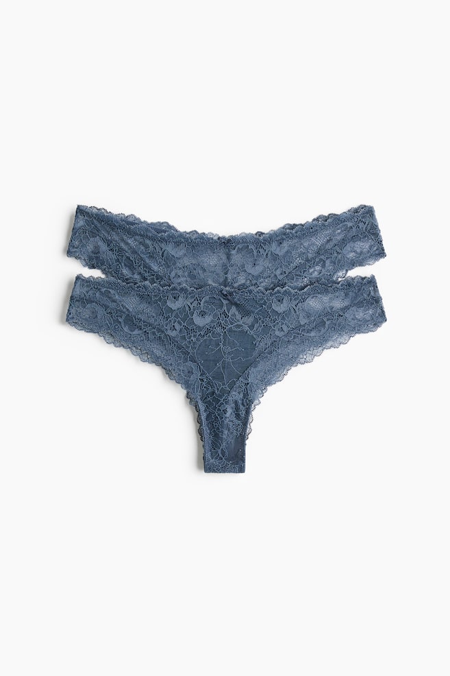 Zwei blaugraue Spitzenstrings liegen flach, wobei einer leicht über dem anderen liegt und ihr Frontdesign zur Schau stellt. Jeder String ist mit einem zarten floralen Spitzenmuster und gewellten Kanten entlang der Taille und Beinöffnungen versehen. - 1