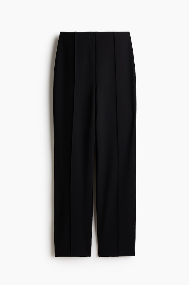 Black trousers are facing front, featuring a flat waistband, straight legs, and vertical pressed creases running down the front of each leg. - 1