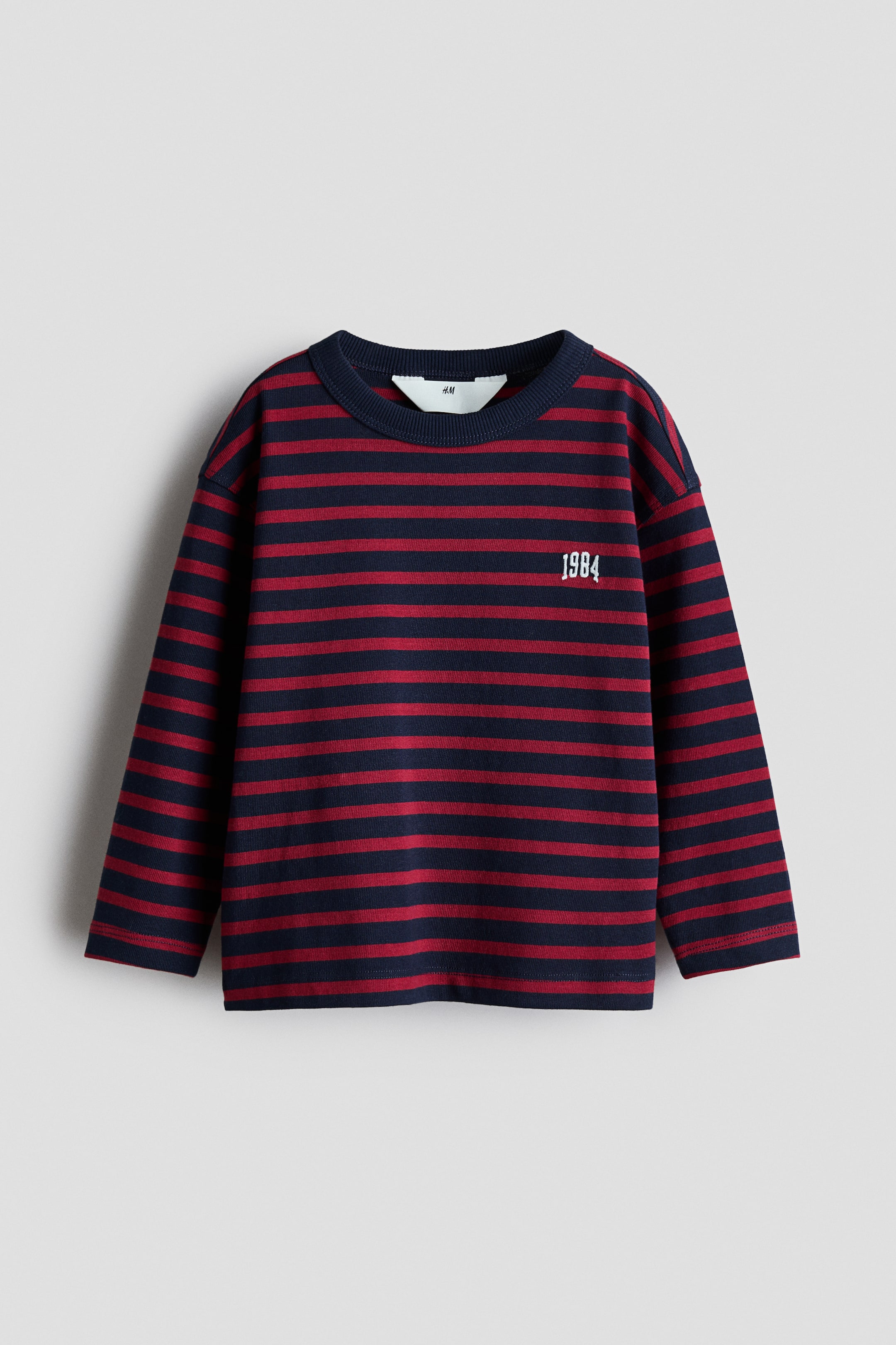 View larger image: A long-sleeved top showcasing horizontal navy blue and red stripes. It features a ribbed crew neck, ribbed cuffs, and the number "1984" embroidered in white on the upper right chest.