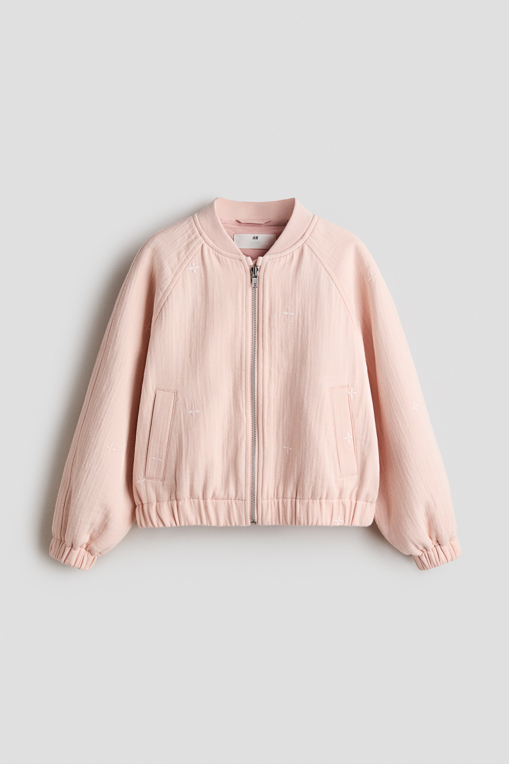 Ver imagen más grande: Una chaqueta bomber rosa se presenta por delante, confeccionada en un tejido de algodón y con motivos bordados. Está diseñada con un cuello bajo acanalado, cierre frontal de cremallera, mangas raglán y bolsillos laterales de ojal, con elásticos cubiertos que rematan los puños y el dobladillo acanalados.