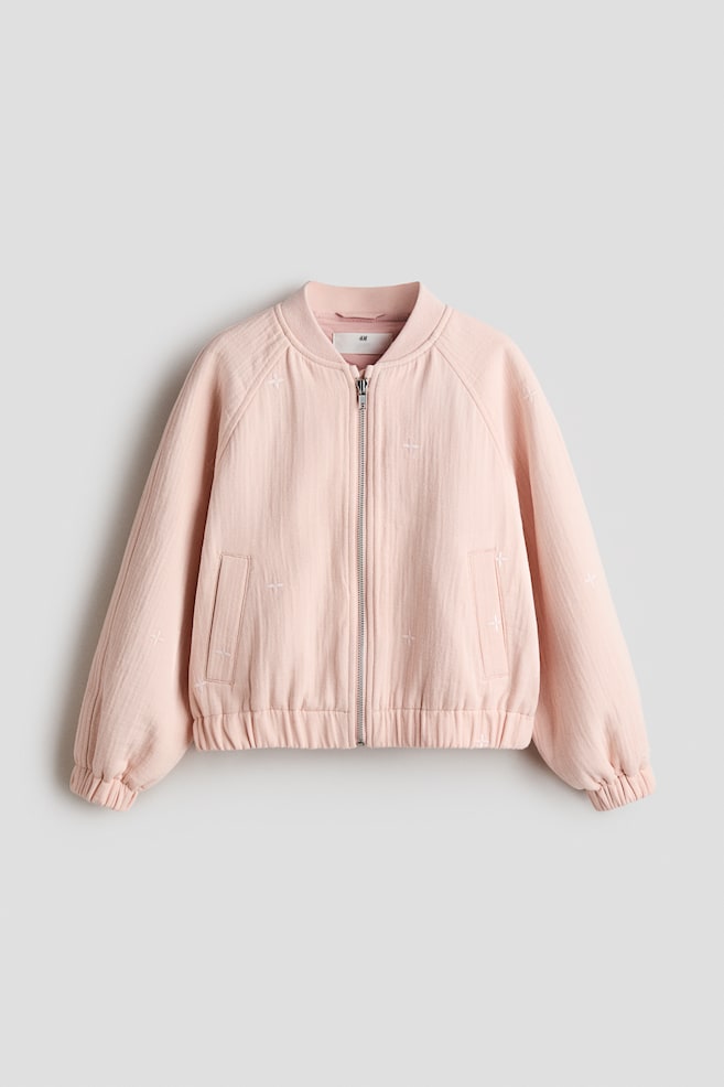 A pink bomber jacket is presenting its front, made from a cotton weave and featuring embroidered motifs. It is designed with a low ribbed collar, a front zip closure, raglan sleeves, and welt side pockets, with covered elastication finishing the ribbed cuffs and hem. - 1