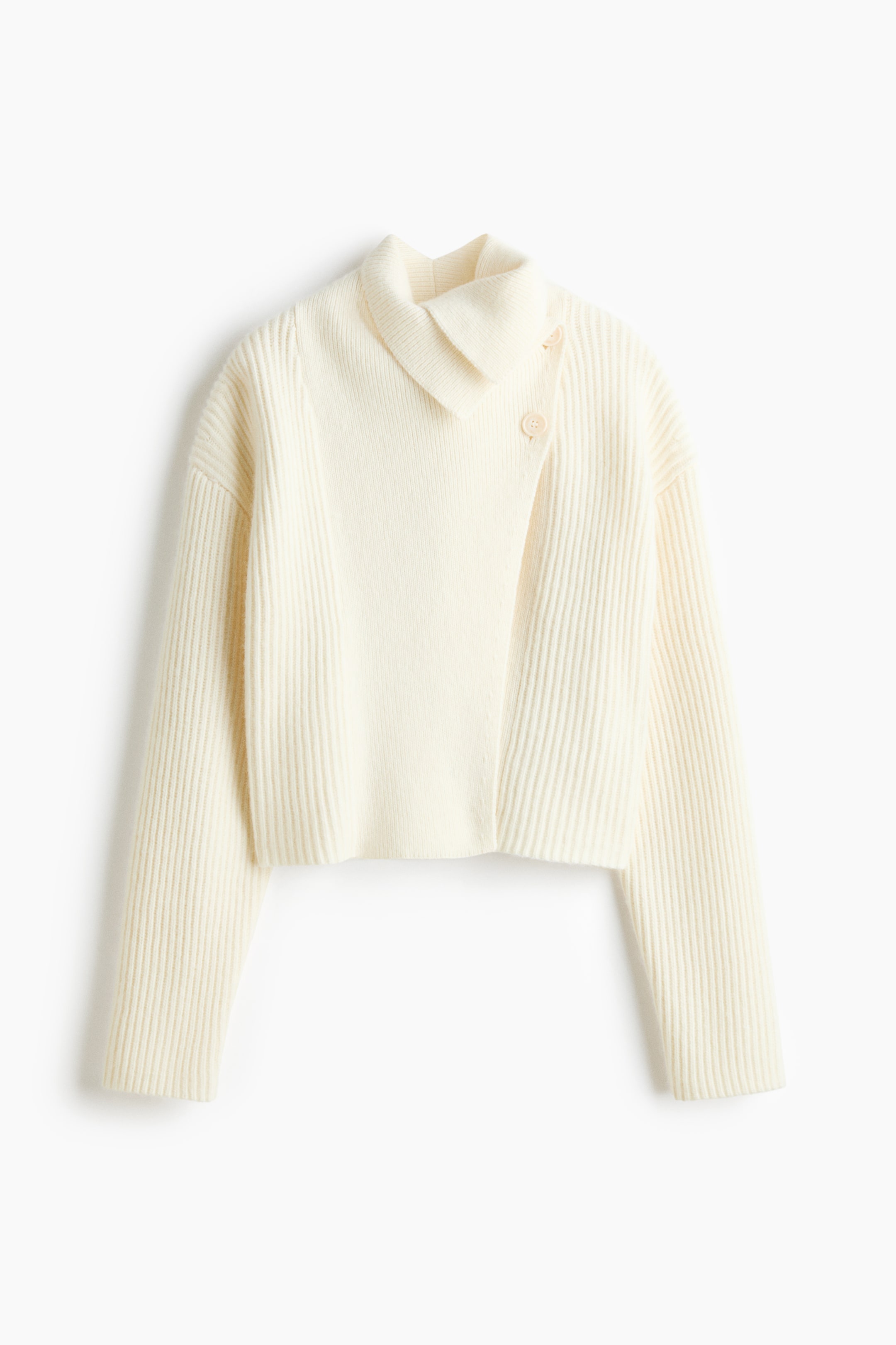 Agrandir l'image: Un pull court en maille blanc cassé est présenté de face, avec une fermeture portefeuille asymétrique sur le devant et deux boutons près du col. Le pull présente une texture côtelée sur l’ensemble, avec un col montant replié et de longues manches amples.