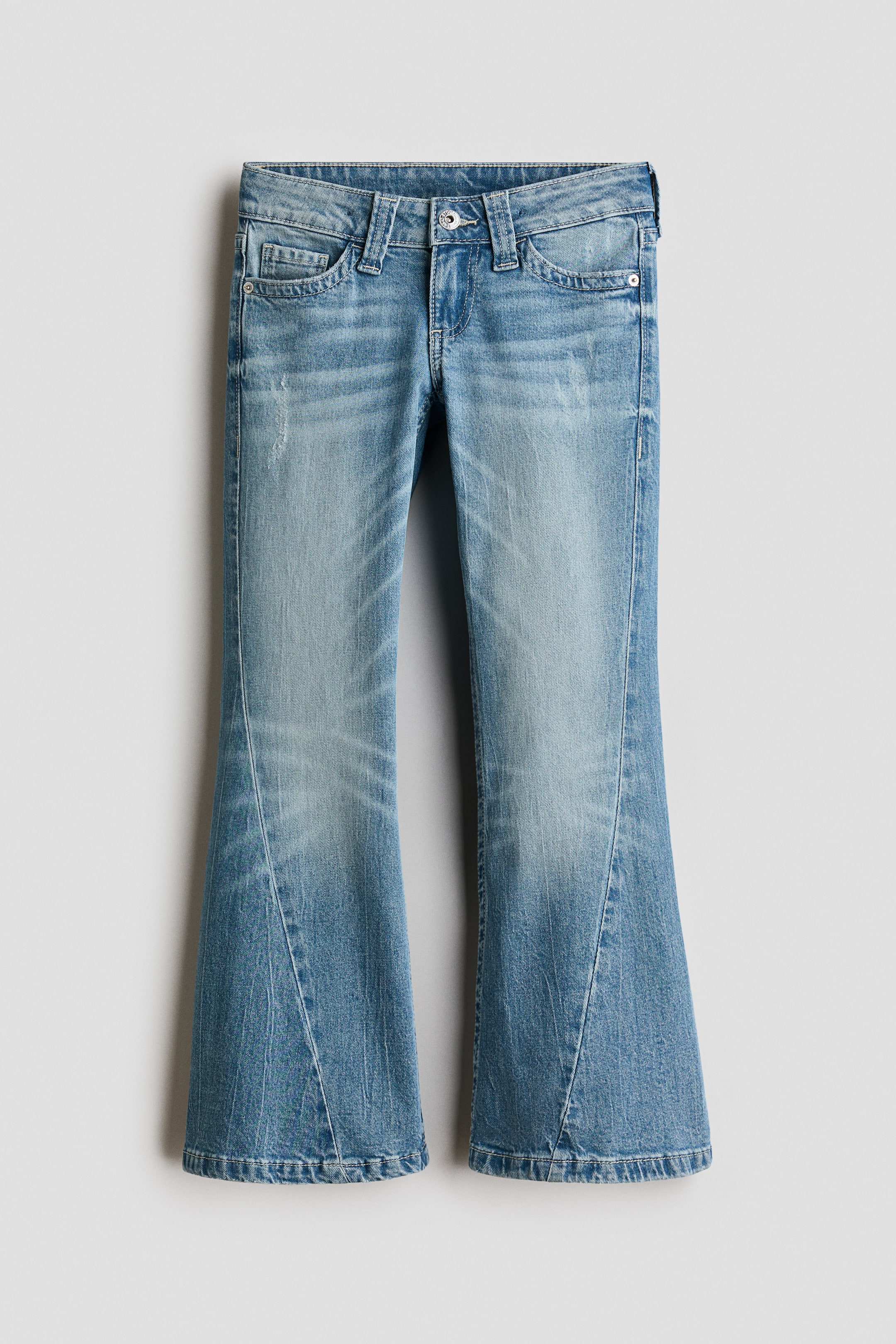 Grotere afbeelding bekijken: Een lichtgewassen denim jeans wordt van voren getoond en laat een flared silhouet zien met opvallende ingezette panelen bij de onderbenen. De jeans heeft vervaging en whiskering op de dijen, samen met een klassieke five-pocket-stijl en een enkele knoopsluiting in de tailleband.