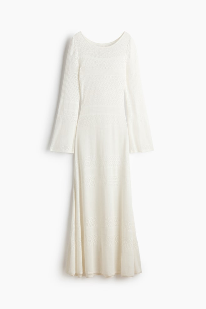 Ein cremeweißes Strickkleid in Midi-Länge ist frontal abgebildet und zeichnet sich durch einen Bootsausschnitt und lange Glockenärmel aus. Es präsentiert eine Vielzahl von Ajourmustern, darunter Rautenmotiven und horizontale strukturierte Bänder, die sich über das figurbetonte Oberteil und den ausgestellten Rock erstrecken. - 1