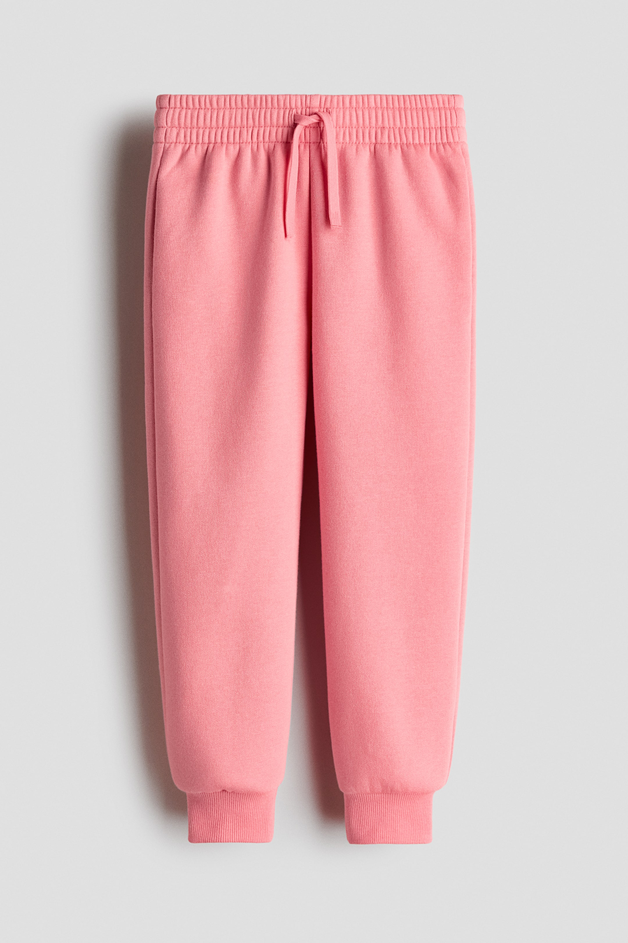 View larger image: Pink sweatpants are presenting as FRONT, featuring a gathered elasticated waistband with a drawstring and ribbed cuffs. The pants are displaying a relaxed fit in a soft, brushed fabric.