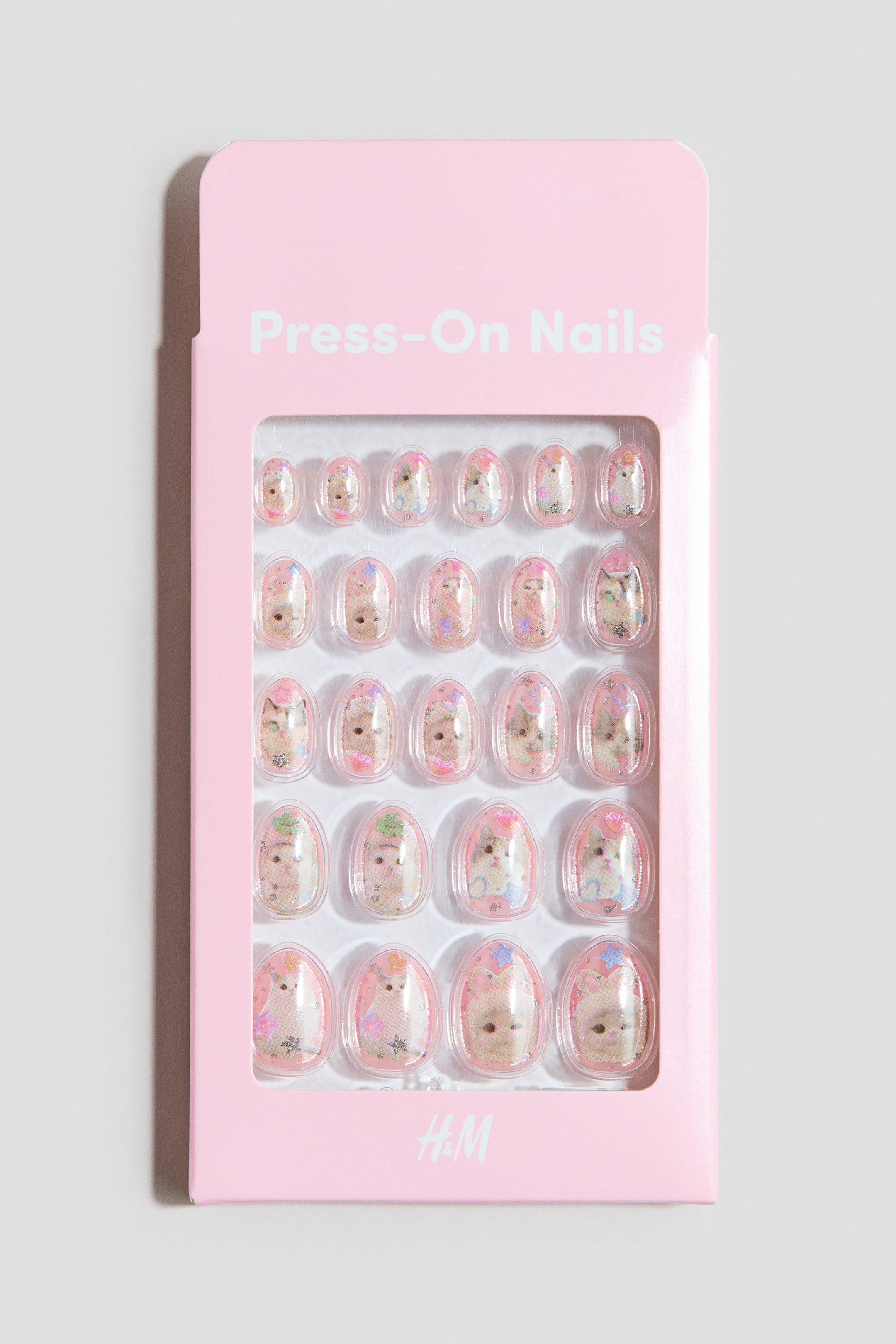 View larger image: The package, presented from the front, features 24 oval-shaped press-on nails in a pink hue. The nails display an array of designs, such as animal faces and glitter, neatly arranged in rows within the transparent packaging.