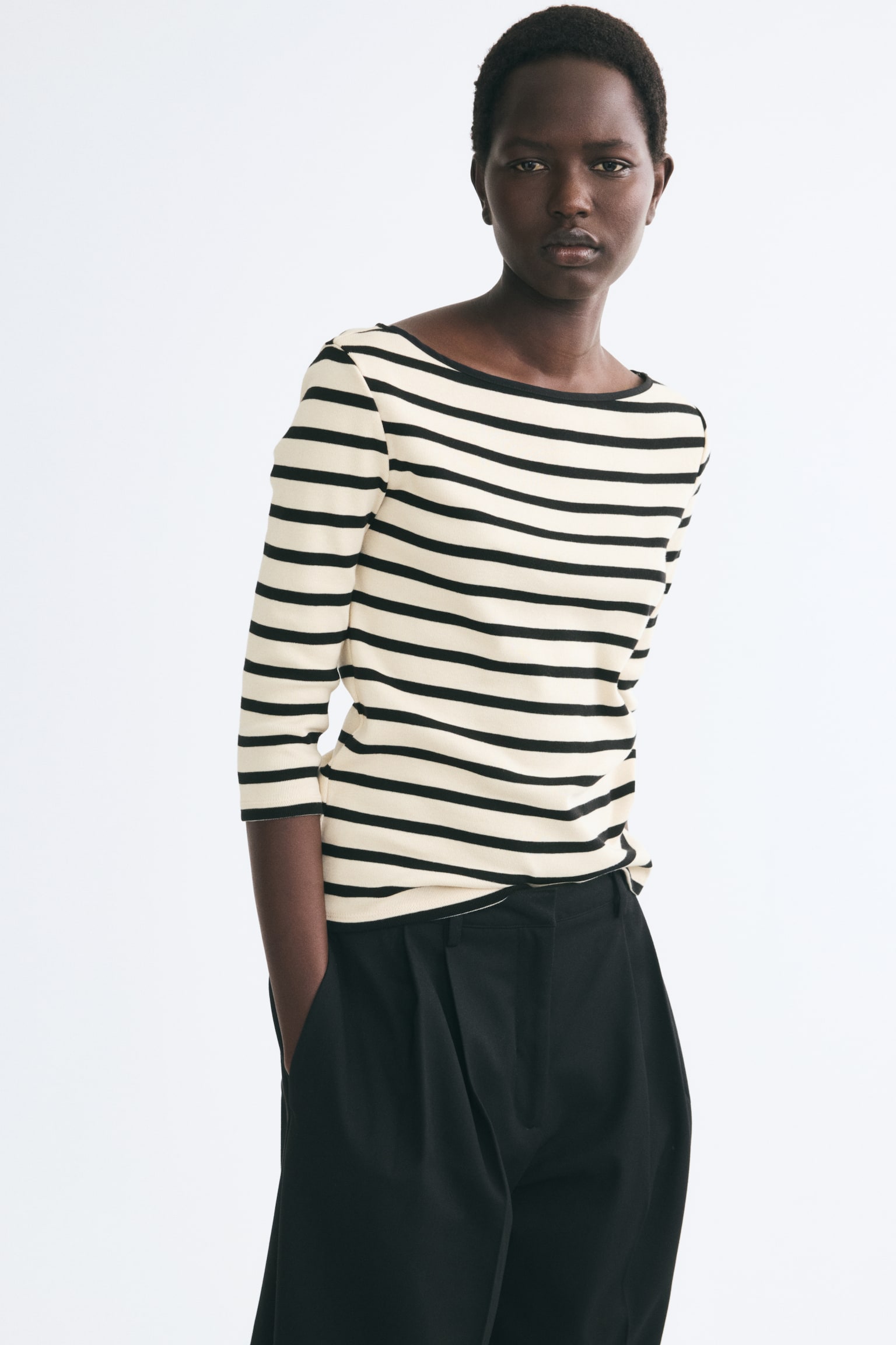 Ein gestreiftes Oberteil ist von vorne zu sehen und zeigt ein horizontal gestreiftes Muster in Beige und Schwarz. Es verfÃ¼gt Ã¼ber einen U-Boot-Ausschnitt mit schmaler schwarzer Einfassung und DreiviertelÃ¤rmel. - 1