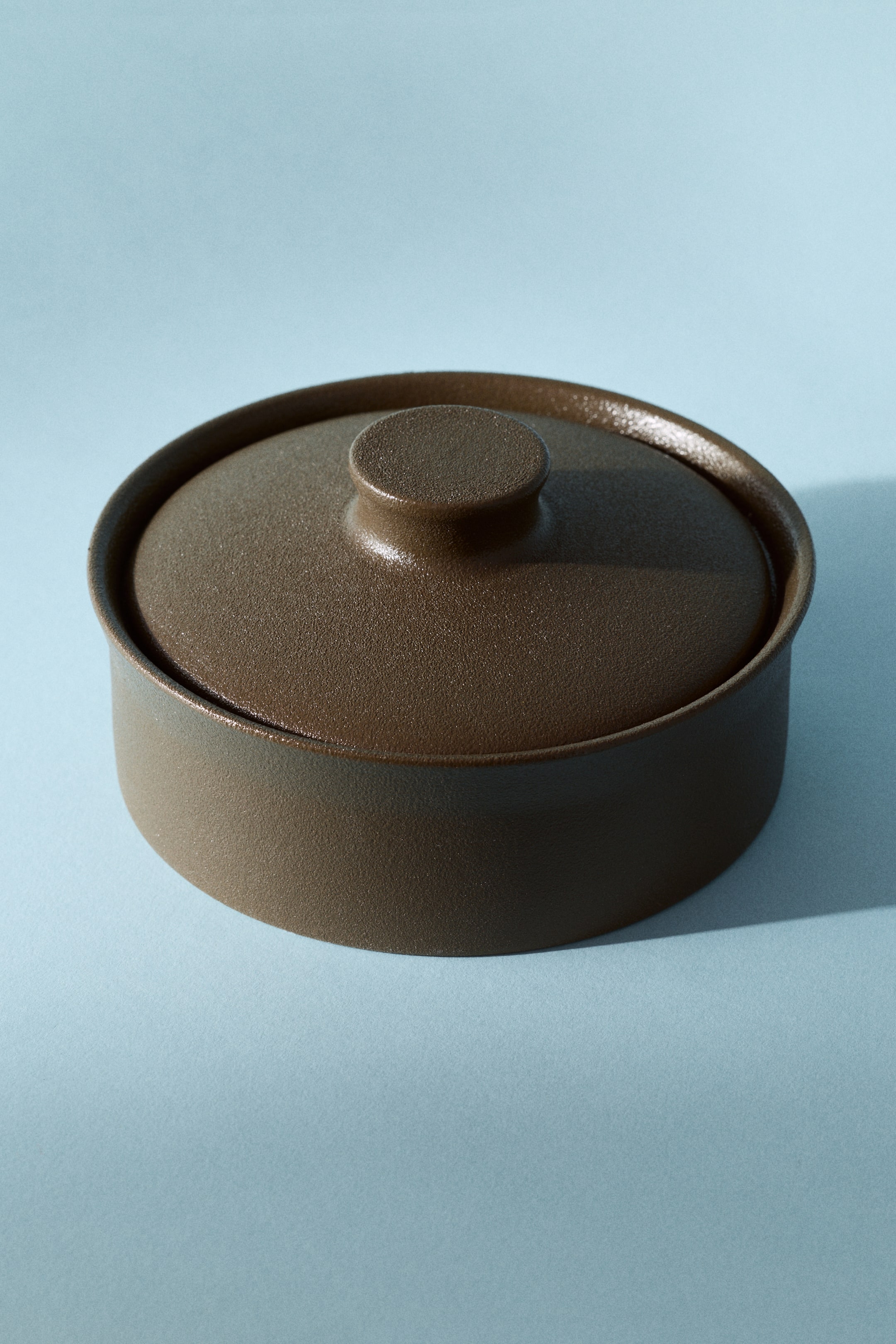 View larger image: A dark brown cylindrical pot is featuring a textured finish. Its matching lid, topped with a small, round knob, is fitting snugly into the pot's opening, all being viewed from a slight top-down angle.