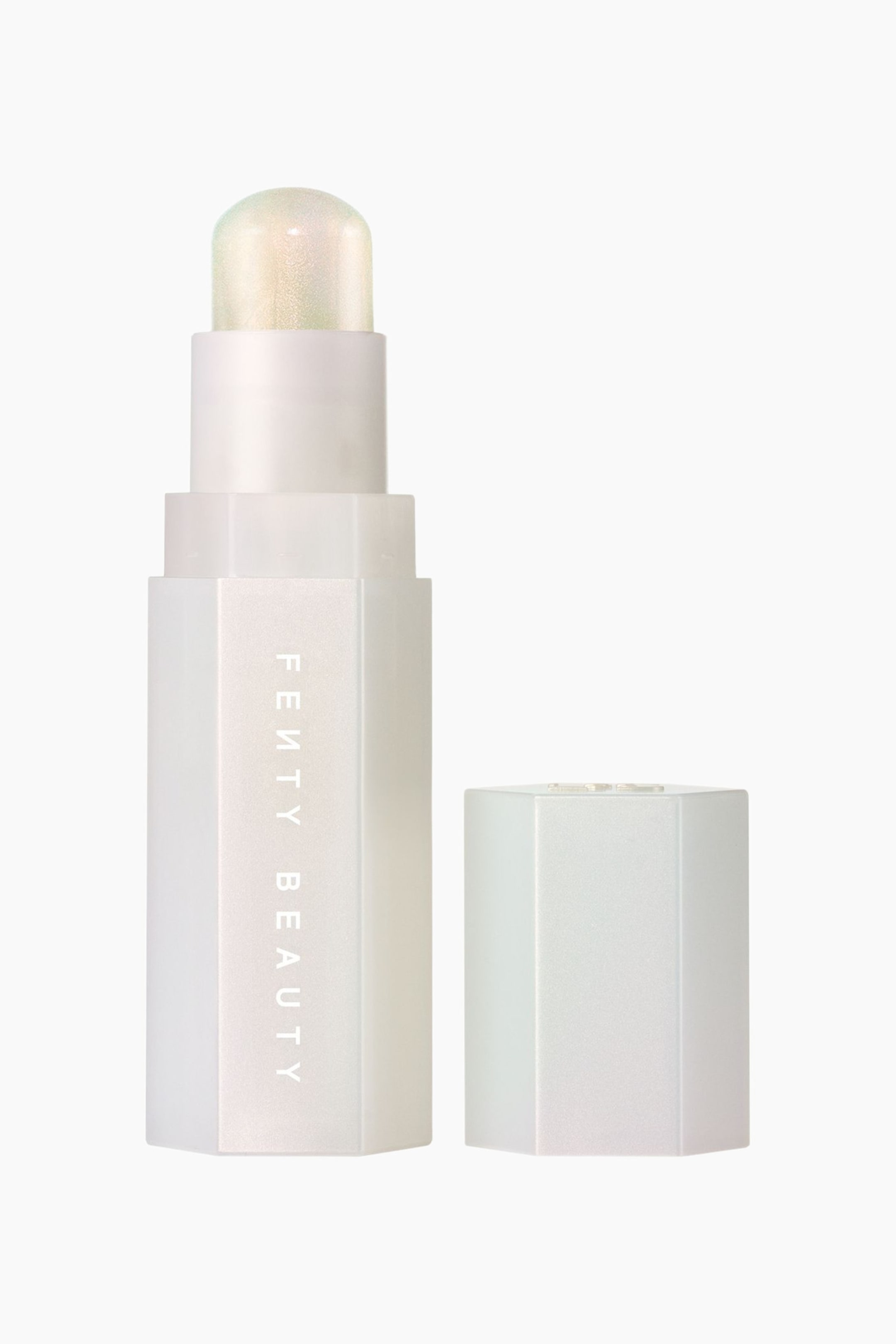 Se større billede: En iriserende, sekskantet makeupstick står oprejst med låget fjernet og fremviser en afrundet kuppel af skinnende, lysreflekterende cream highlighter. Den perlemorshvide beholder har brandnavnet "FENTY BEAUTY" trykt lodret og er placeret ved siden af det matchende sekskantede låg.