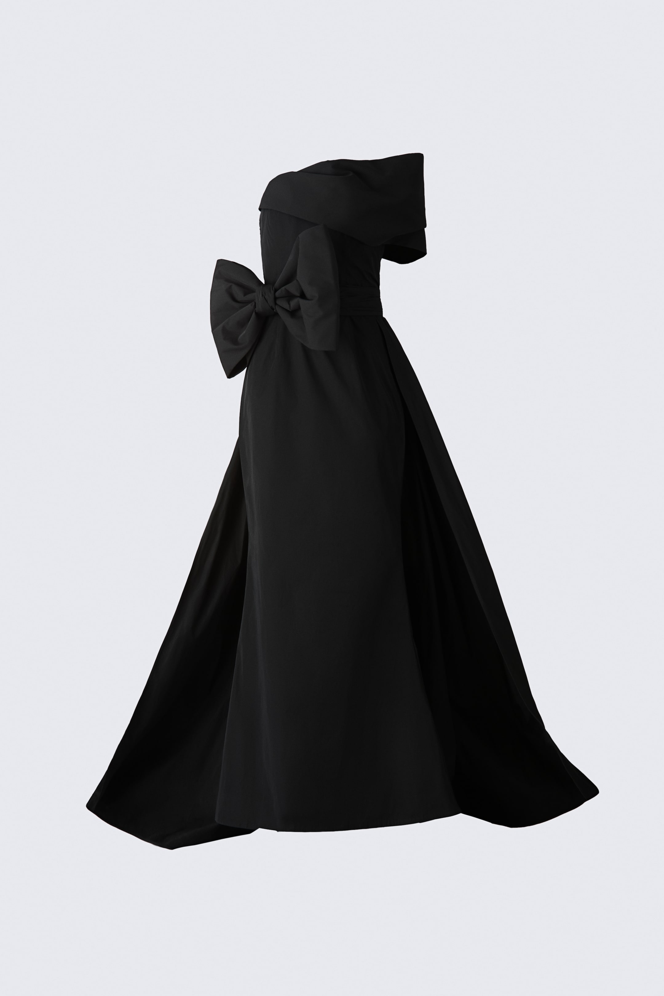 Ver imagen más grande: Se muestra un vestido bandeau negro hasta el suelo desde un ángulo lateral de tres cuartos, resaltando su silueta estructurada. El vestido presenta un panel de manga drapeada con hombros descubiertos, un gran lazo a juego en la cintura lateral y una falda amplia acampanada con una cola dramática.