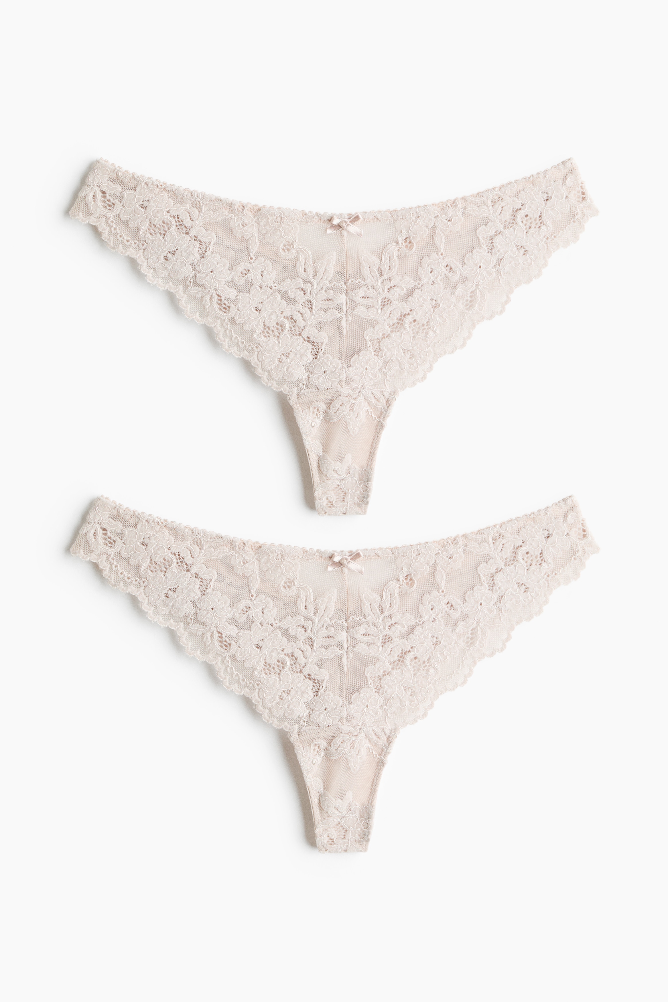 Il modello indossa uno slip tanga in rete ricamata rosa chiaro, caratterizzato da vita bassa e da un piccolo fiocco decorativo al centro. Il prodotto è abbinato a un bralette a triangolo in pizzo coordinato.