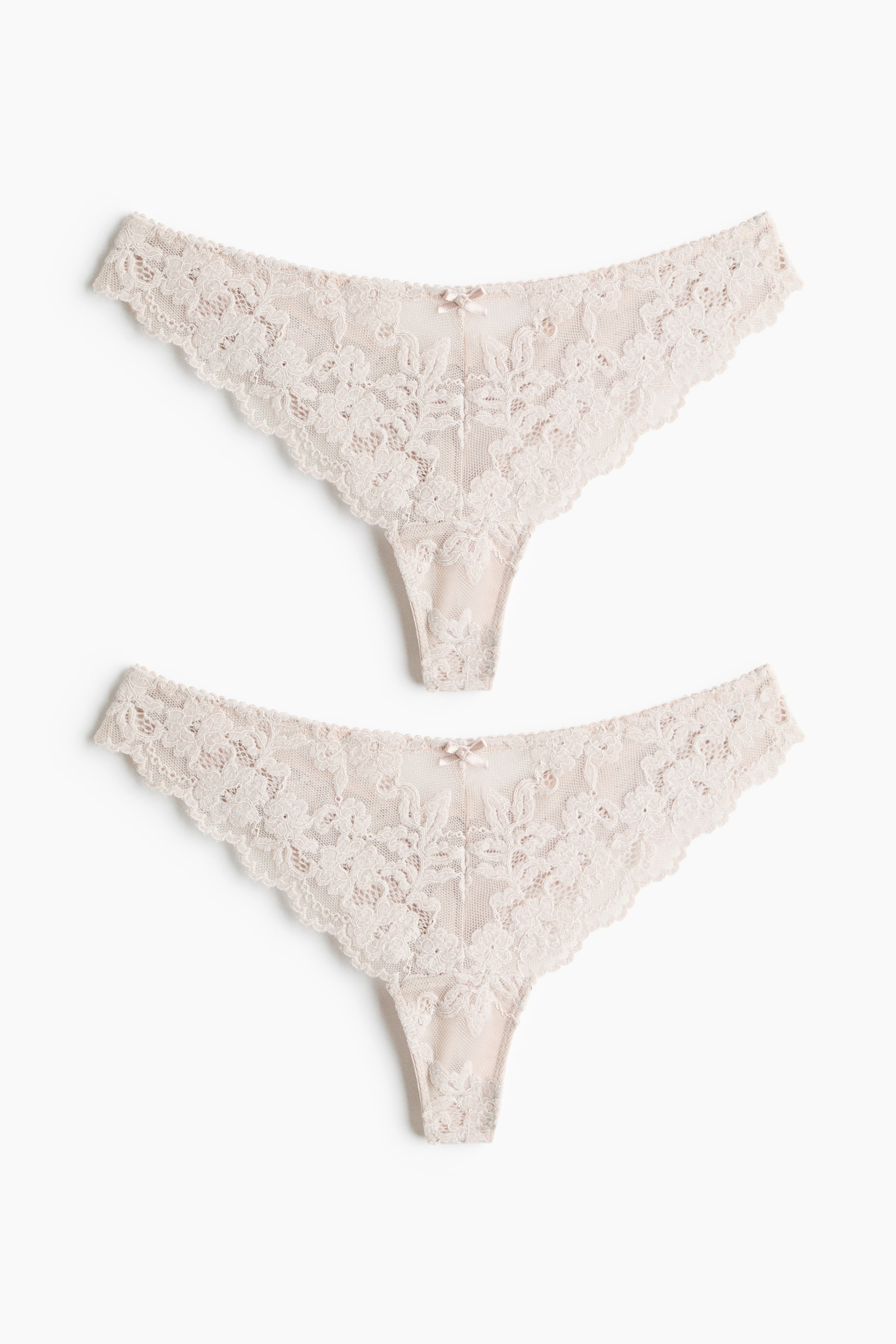 Visualizza immagine più grande: Slip tanga in mesh ricamato mostrati frontalmente in un set di due, disposti uno sopra l’altro. Ogni paio a vita bassa presenta un pizzo floreale trasparente con bordi smerlati e un piccolo fiocco decorativo al centro della cintura sul davanti.