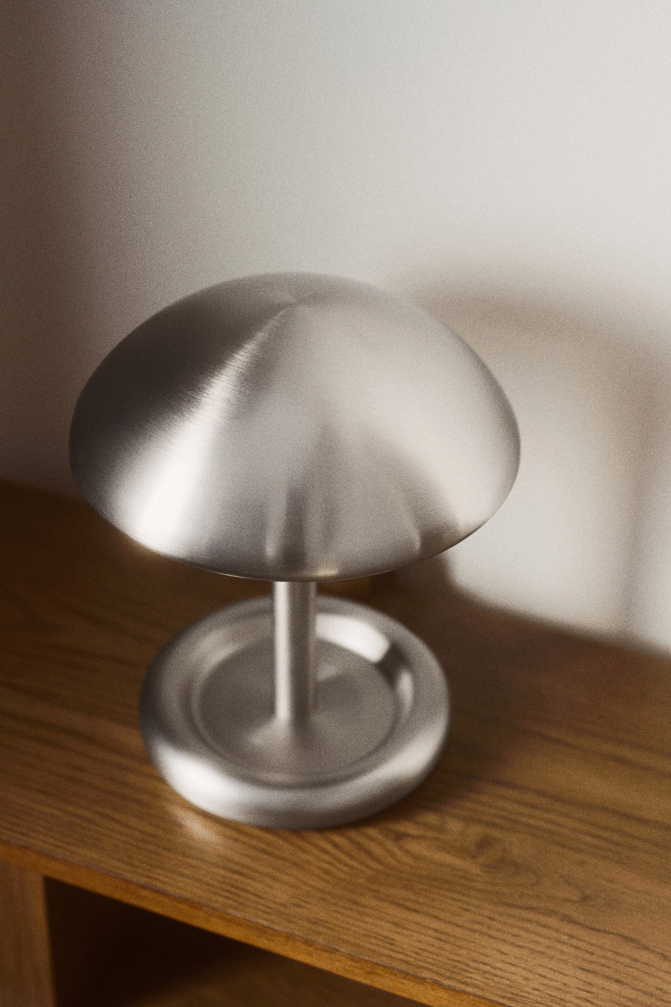 View larger image: A brushed metal table lamp featuring a domed lampshade with gently rounded edges, mounted on a sleek stem. This stem connects to a circular base, also showcasing gently rounded edges.