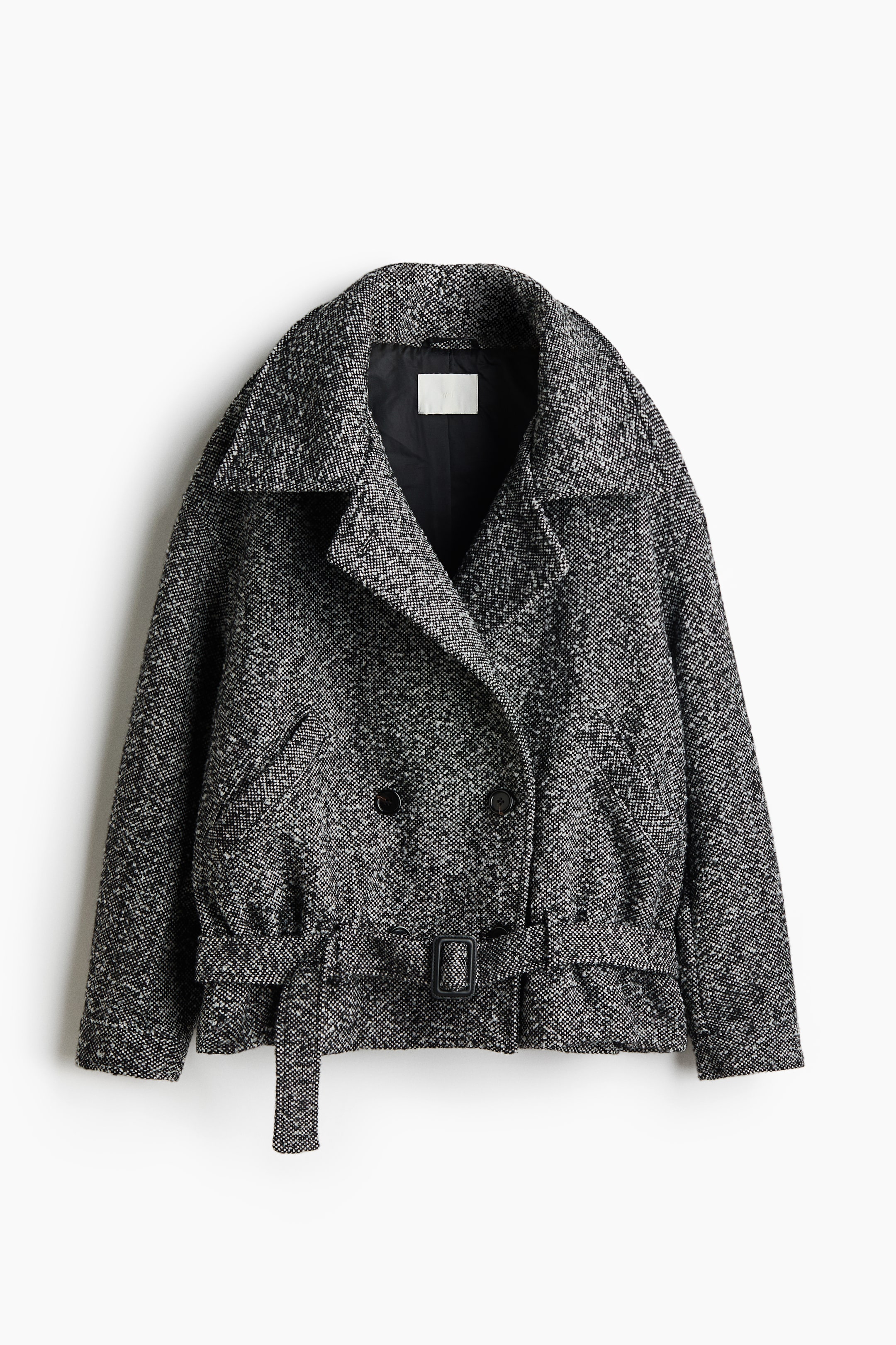 View larger image: A black-and-white textured tweed jacket is shown from the front, featuring wide notch lapels and a double-breasted front with dark buttons. The jacket is styled with a matching fabric belt and black buckle at the hem, slanted welt pockets, and a black interior lining.
