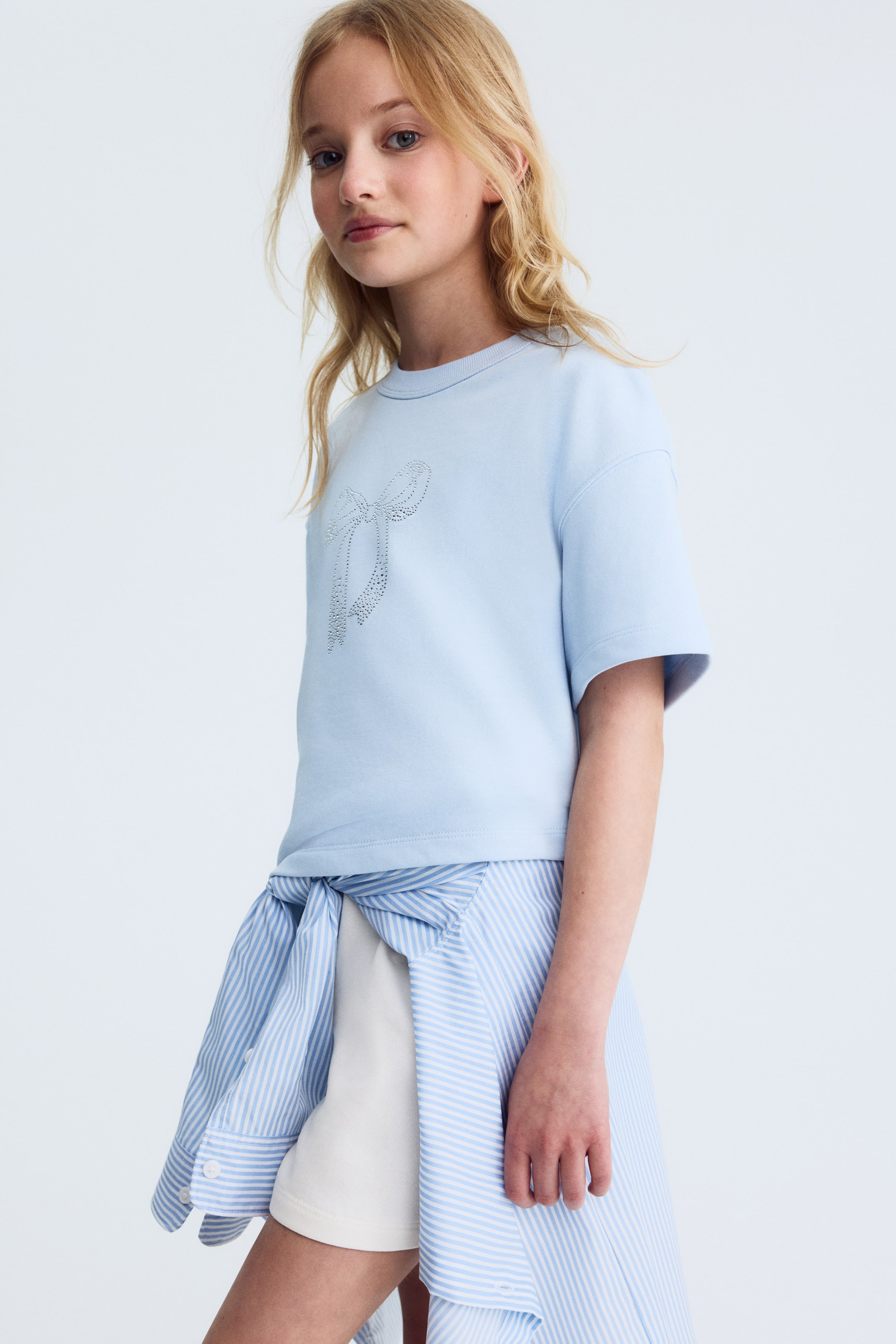 View larger image: Light blue T-shirt in soft jersey crafted from a cotton blend, showcasing a round, ribbed neckline, relaxed shoulders, and a dazzling bow detail on the front.