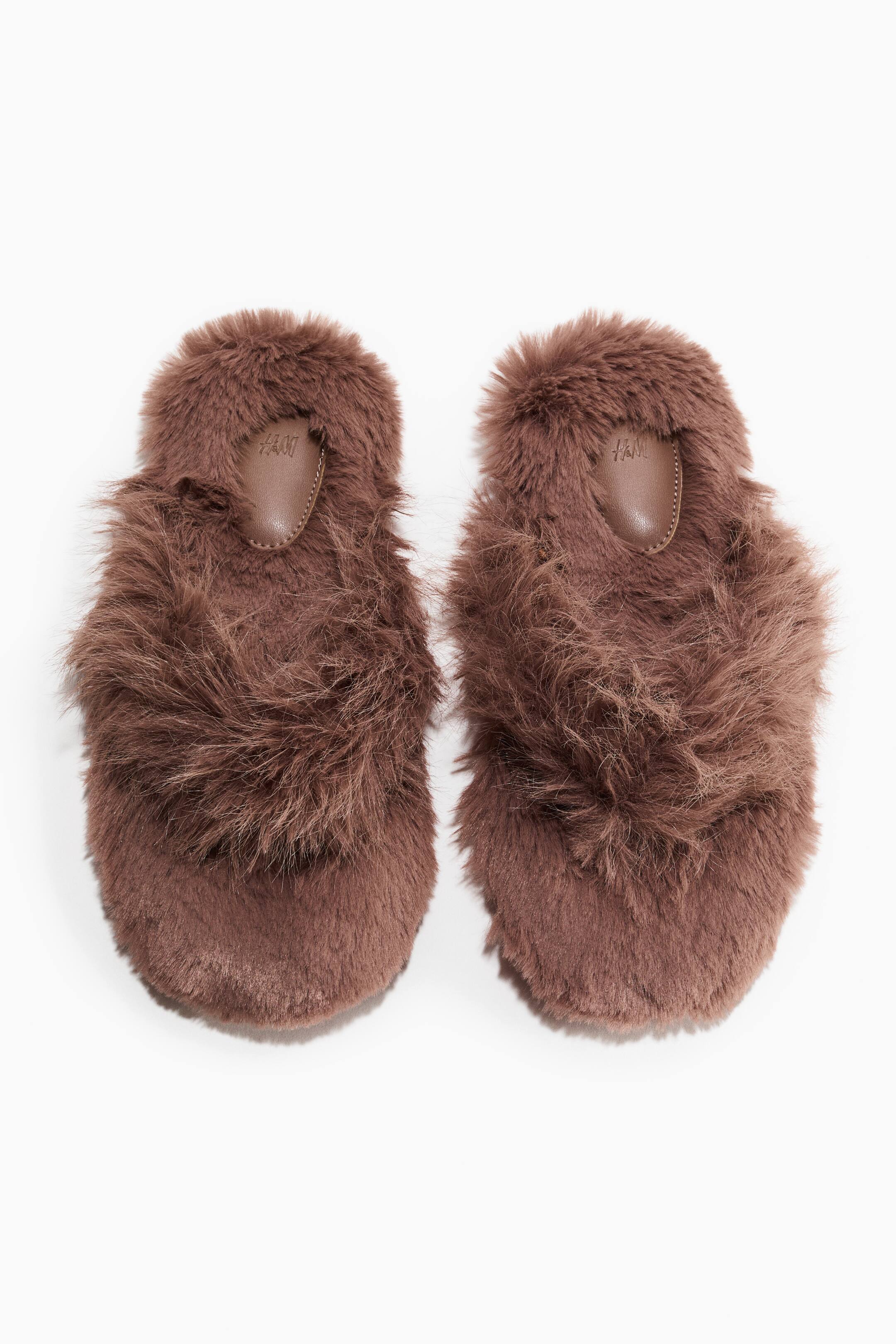 Se større billede: Et par brune, fluffy hjemmesko ligger side om side og viser en langhåret, pjusket faux-fur-struktur over hele overdelen og fodsengen. En glat, brun, dråbeformet hælpude hviler på indlægssålen i hver hjemmesko.
