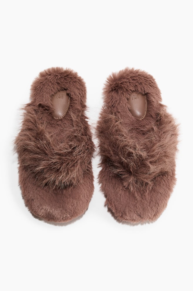 A pair of brown fluffy slippers is lying side-by-side, displaying a shaggy, long-pile faux-fur texture across the entire upper and footbed. A smooth, brown teardrop-shaped heel pad is resting on the insole of each slipper. - 1