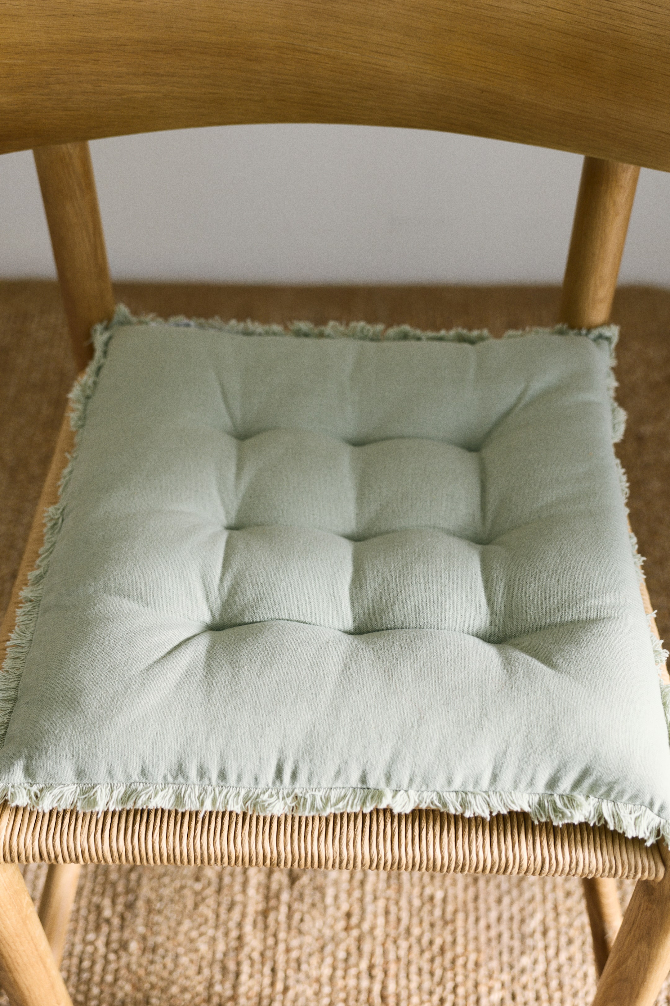View larger image: A set of padded seat cushions features a light green linen and cotton blend, with quilt knots forming a grid pattern across the surface and frayed edges along the perimeter.