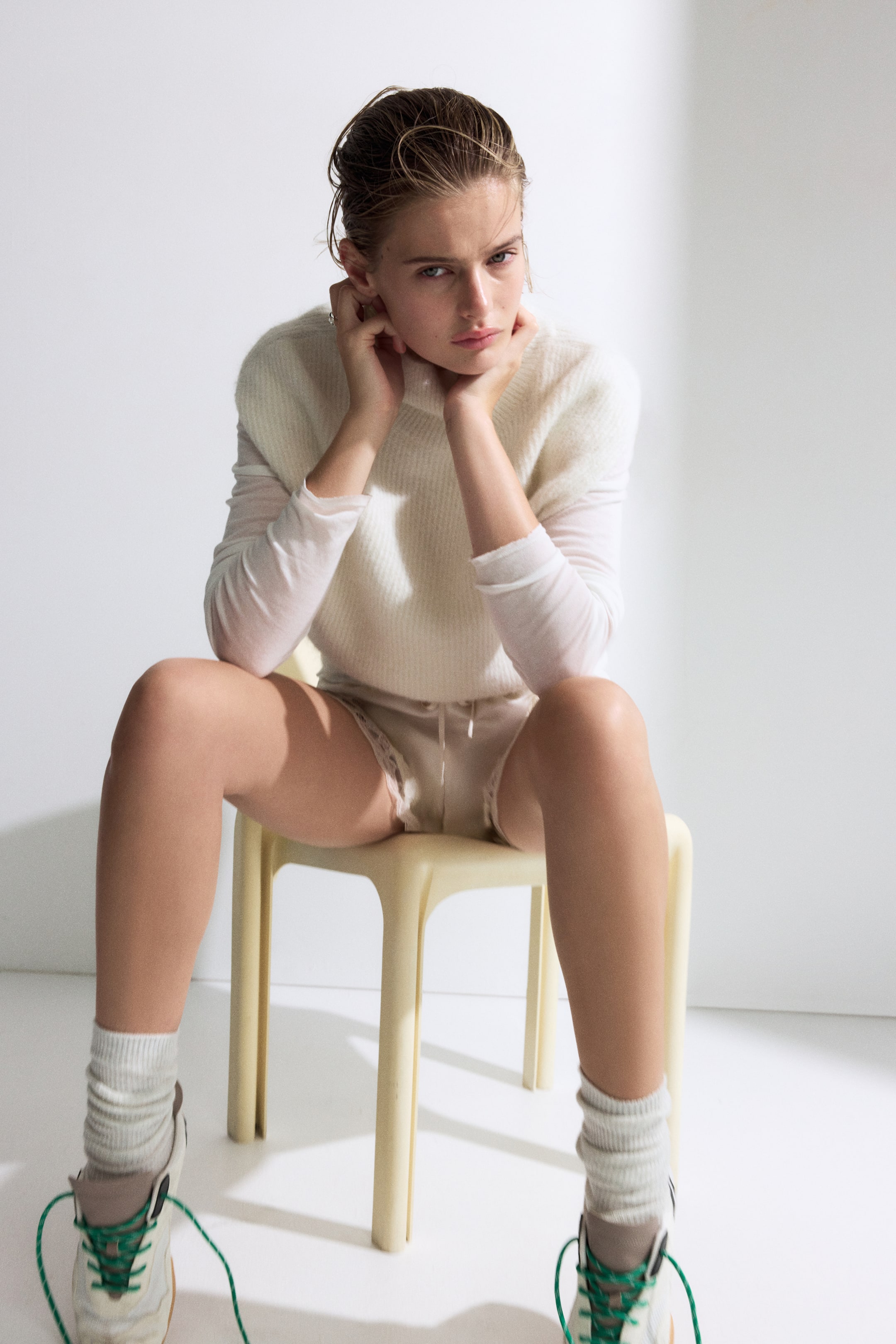 Agrandir l'image: Un gilet en maille coupe ample, de couleur crème, avec un col montant et un ourlet côtelé, porté par le mannequin. Le gilet présente une finition douce et texturée et est superposé à un haut blanc transparent à manches longues.