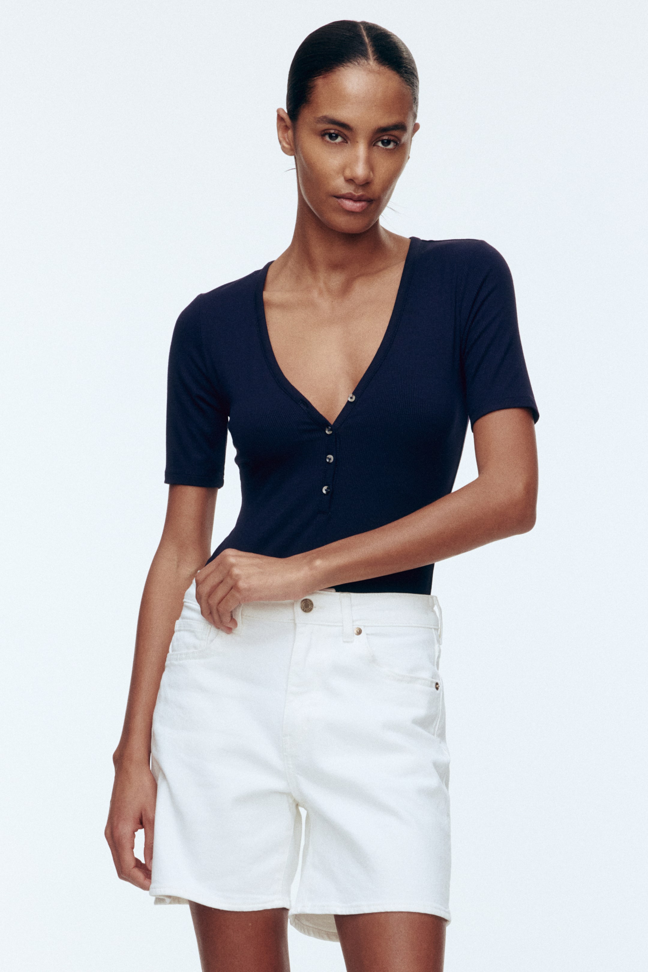 Ampliar la imagen: Un top tejido acanalado de color azul marino presenta un escote en V, mangas cortas y una tapeta de botones en la parte delantera. Queda ajustado al torso.