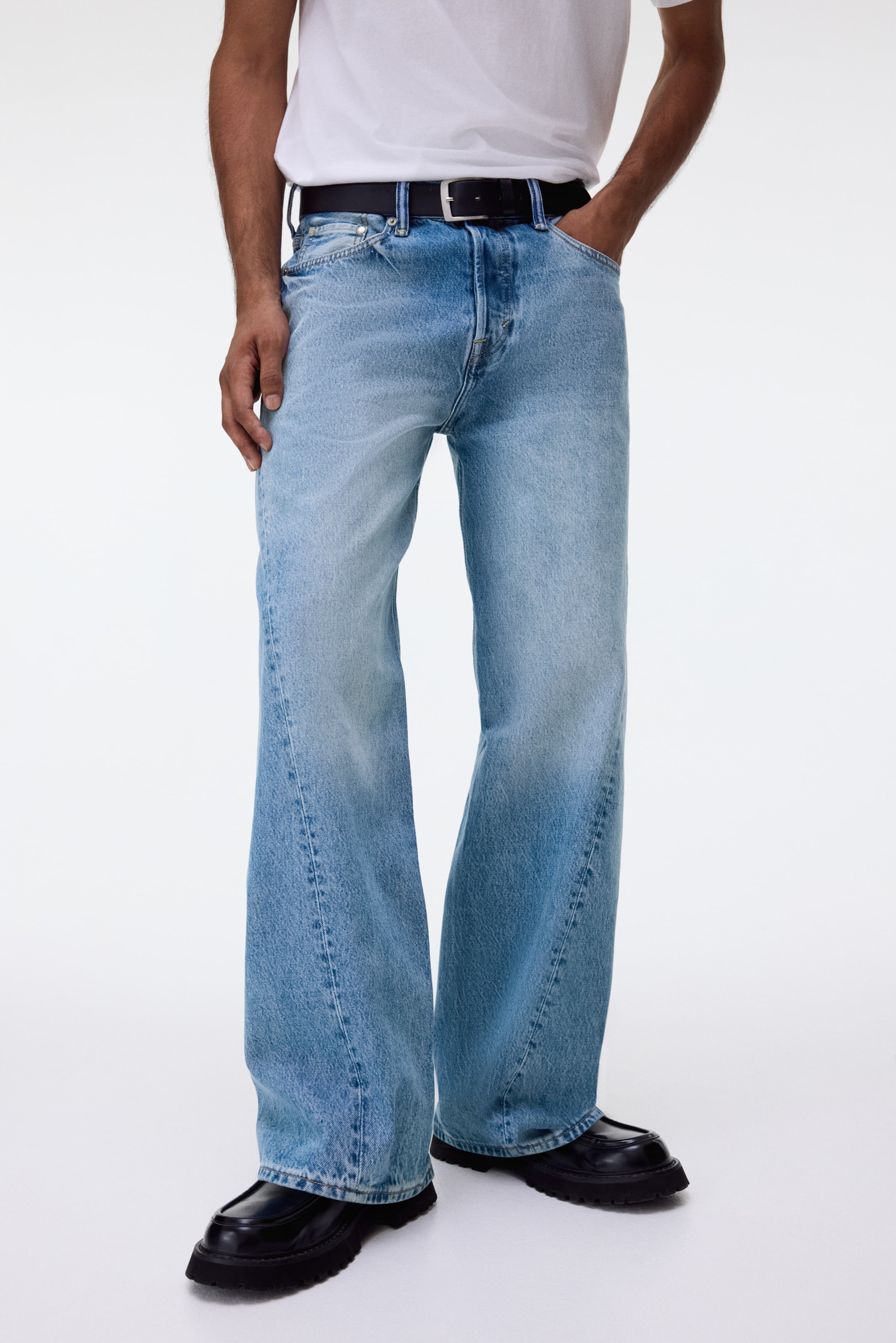 View larger image: Light blue wide-leg jeans feature a faded wash with lighter areas on the thighs and prominent vertical front seams, presenting a relaxed fit. They are styled with a black belt and are shown from the front, draping over black shoes.