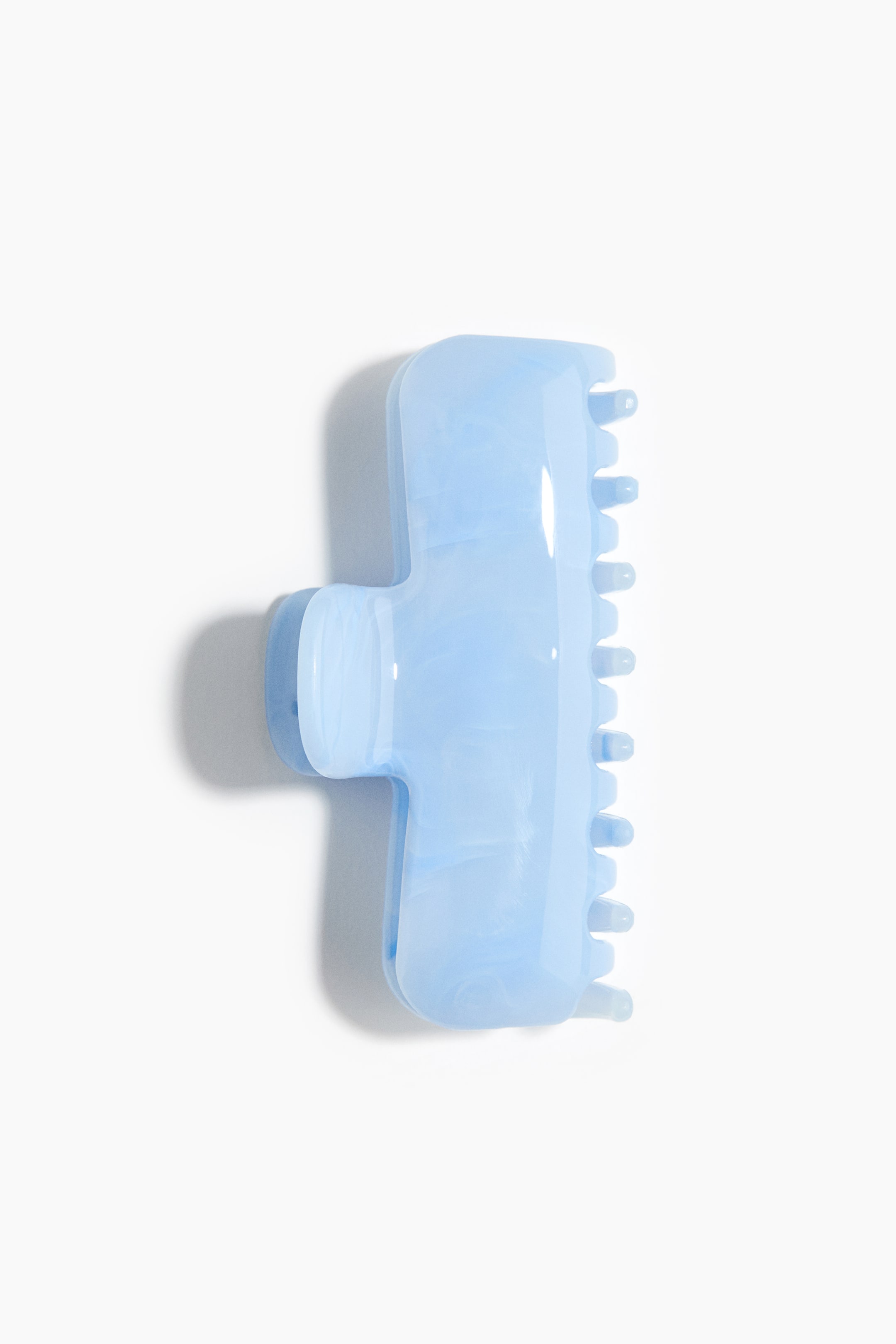 View larger image: A T-shaped hair claw, made from shiny light blue plastic, features a hinged section and rounded teeth along one side, with a subtle marbled pattern visible throughout its material.
