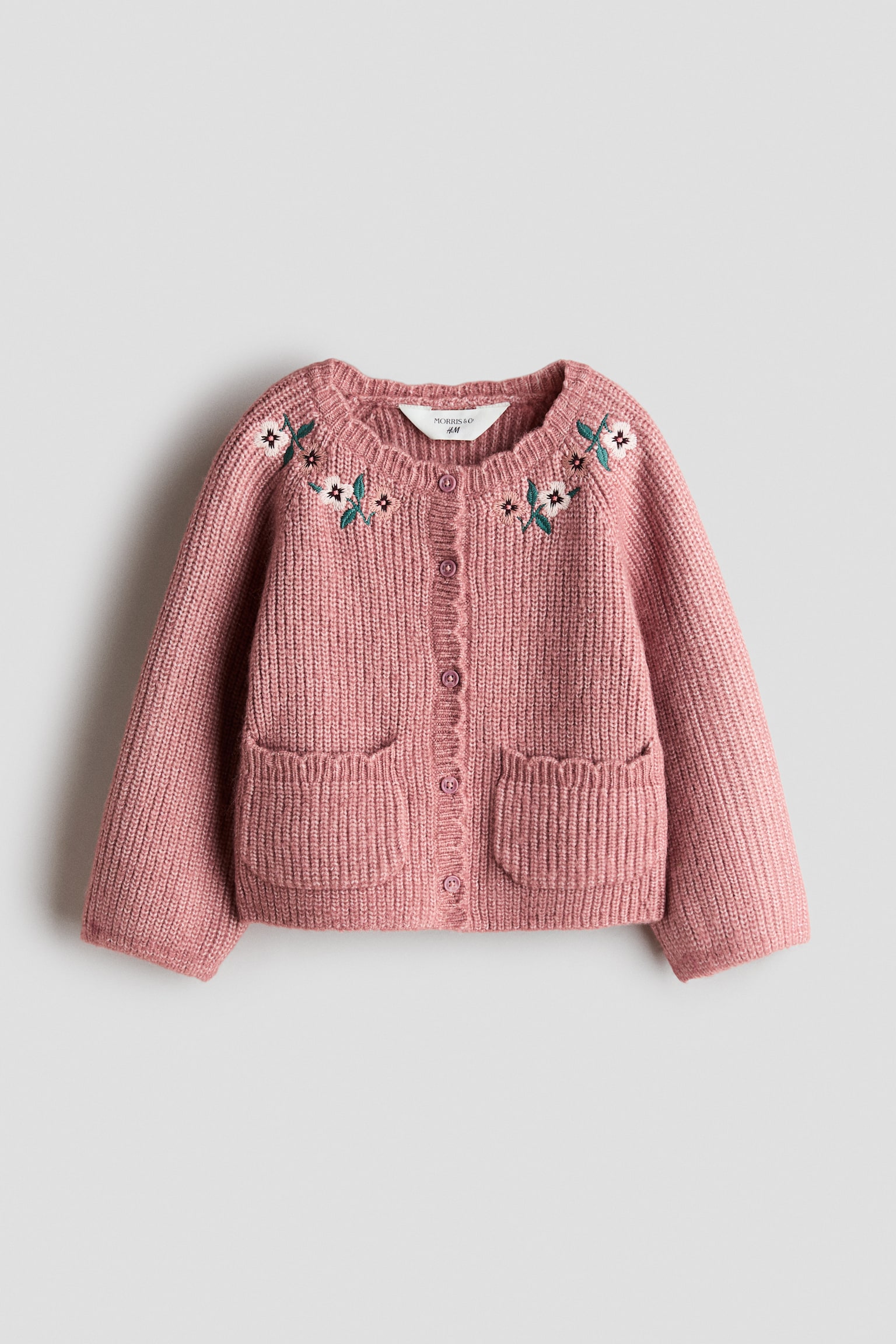 Un cardigan en maille rose est prÃ©sentÃ© de face, avec un col rond festonnÃ©, une fermeture boutonnÃ©e sur le devant et deux poches plaquÃ©es ouvertes Ã  lâavant, avec finitions festonnÃ©es. Le cardigan prÃ©sente des dÃ©tails floraux brodÃ©s blancs et verts sur le haut de la poitrine et les Ã©paules. - 1
