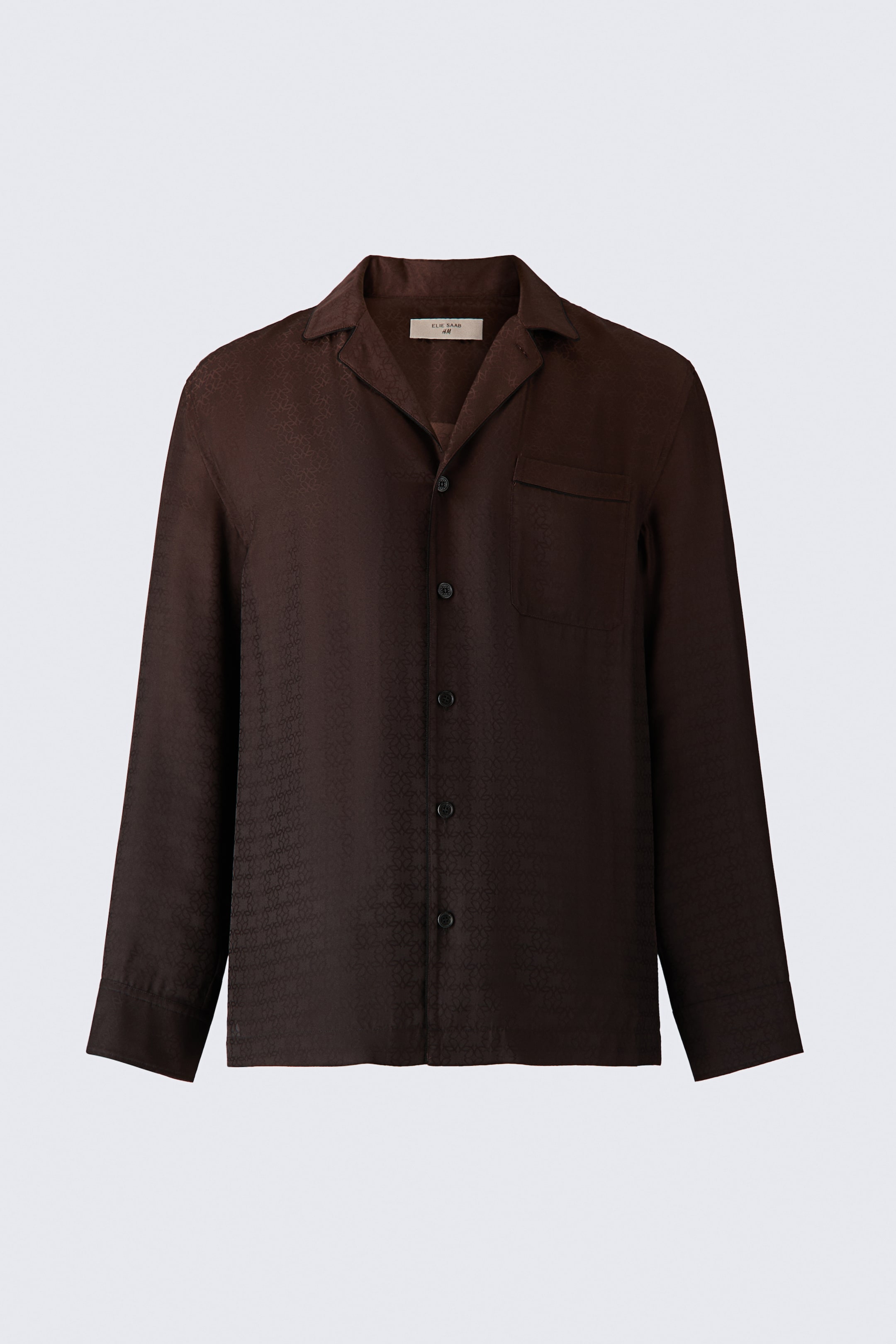 View larger image: A dark brown, long-sleeved pyjama shirt featuring a subtle monogram pattern in jacquard satin is shown from a front-facing perspective. The shirt is designed with a resort collar, a button-down front, a single patch pocket on the left chest, and buttoned cuffs.