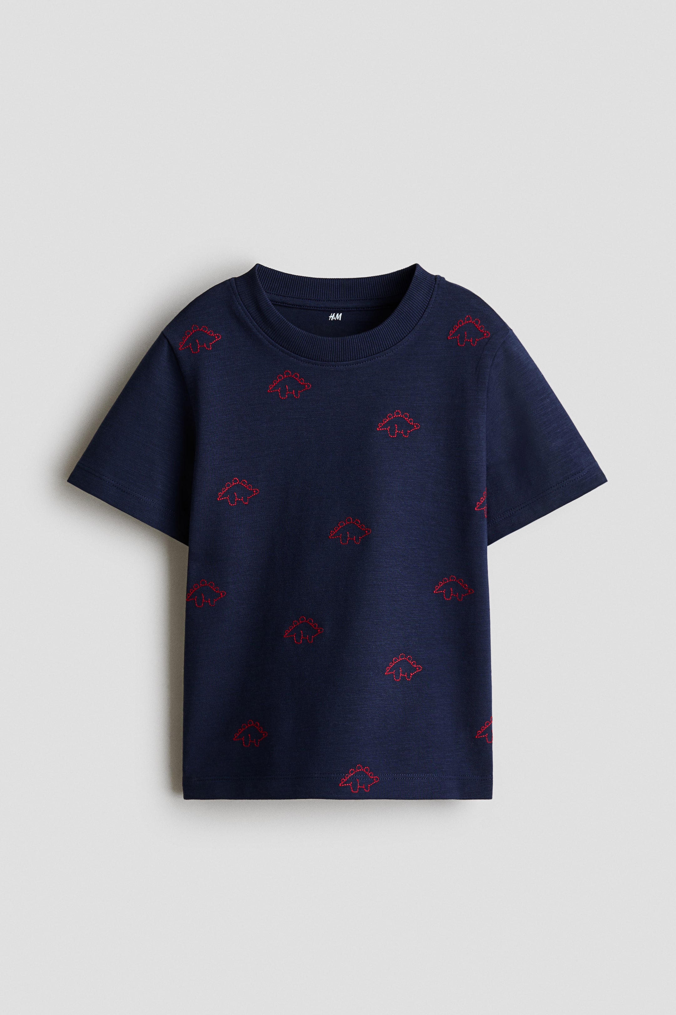 View larger image: A navy blue T-shirt is shown from the front, featuring an all-over pattern of small red embroidered dinosaur outlines, a ribbed crew neck, and short sleeves.