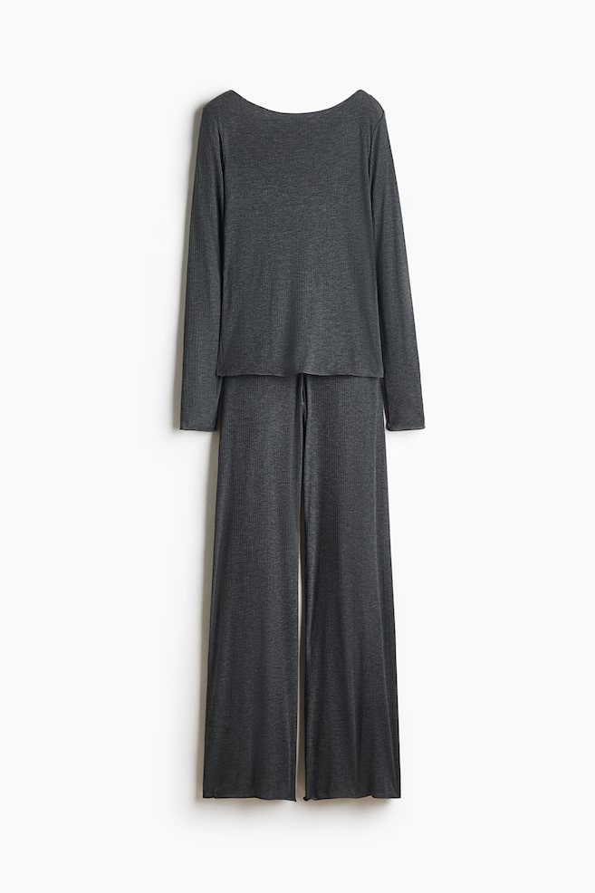 A dark grey pyjama set is hanging flat, facing front, featuring a long-sleeved top with a boat neckline and matching wide-leg pants in a sheer, ribbed jersey fabric. Both pieces are showcasing overlocked edges at the cuffs and hems. - 1