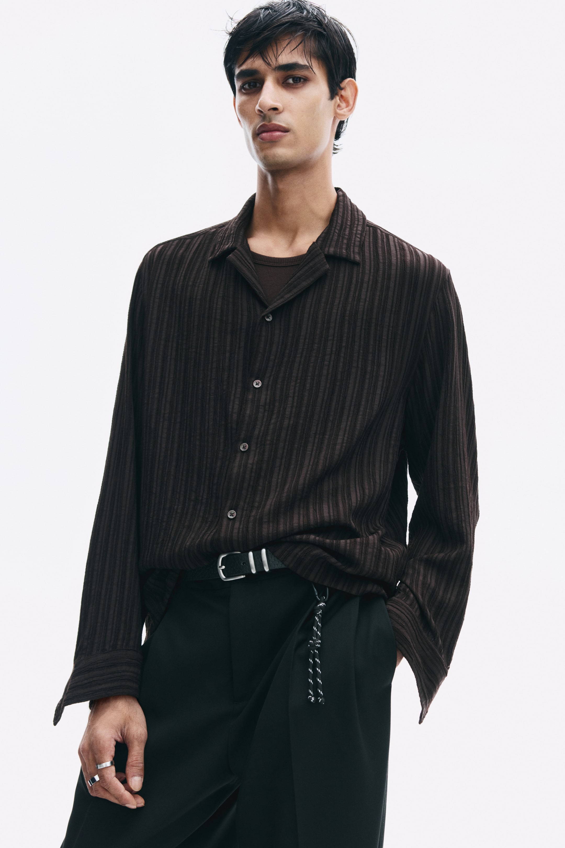 View larger image: A dark brown, vertically textured long-sleeve shirt with a resort collar and button-front closure is being worn by the model. The relaxed-fit shirt is layered over a dark t-shirt and partially tucked into black trousers.